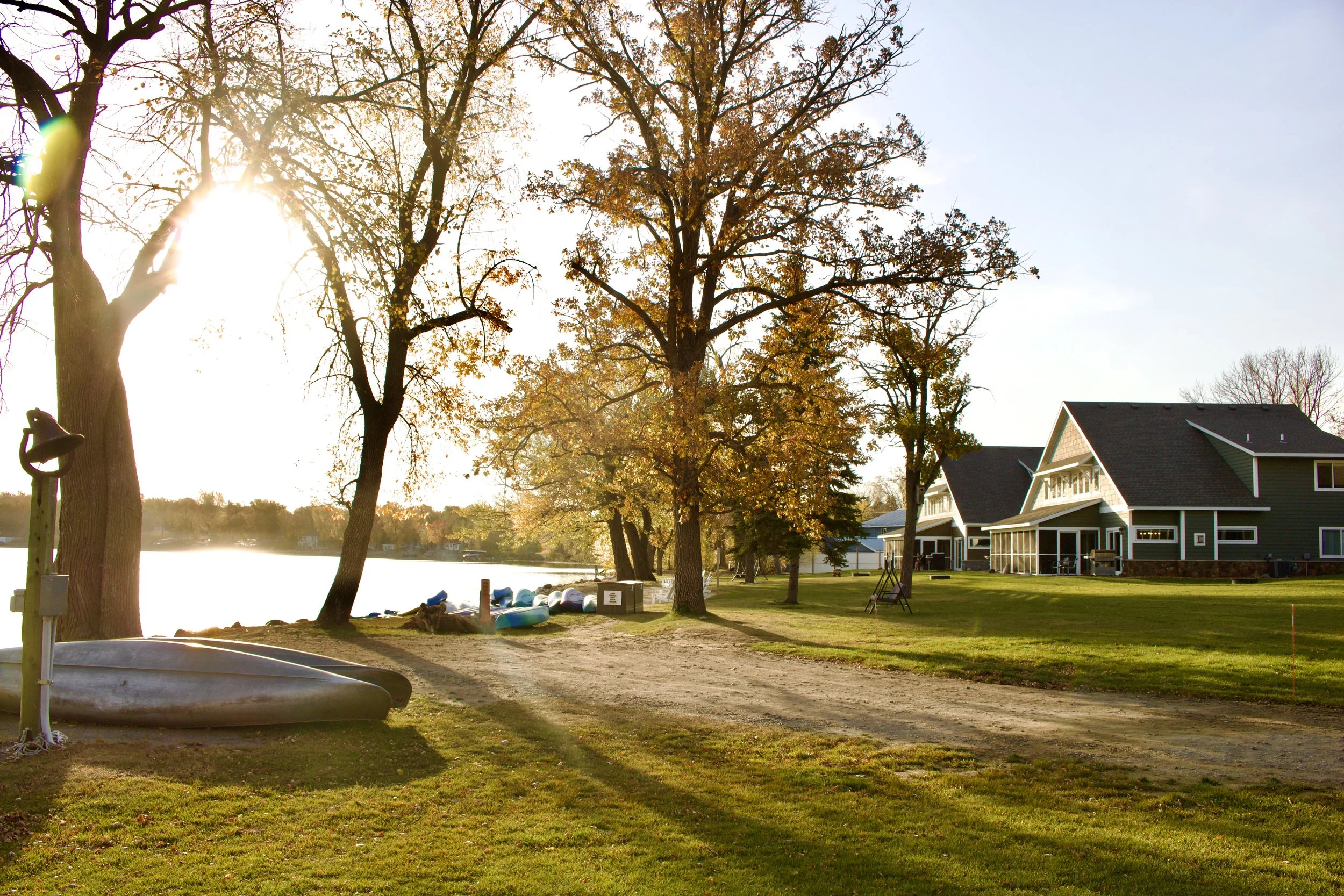 Low autumn sun through the trees on the resort lawn at Lake Darling, kayaks turned over on the grass and villas along the shoreline