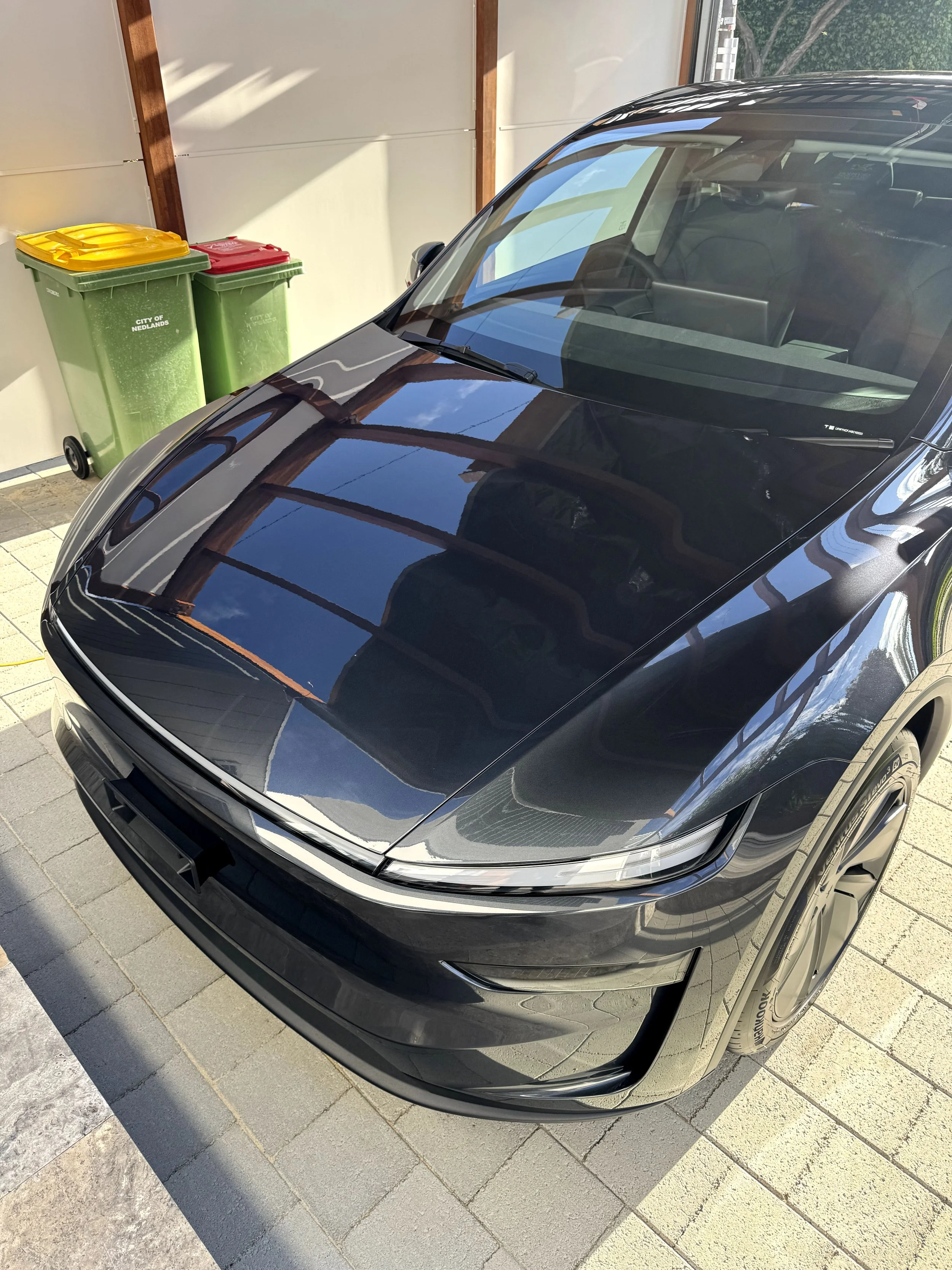 Black Tesla car parked indoors with reflections of the ceiling and windows on the hood.