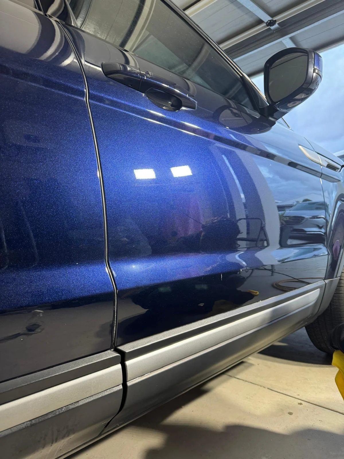 Close-up of a blue car door with a crack running down the center, showing a metallic finish and a side mirror.