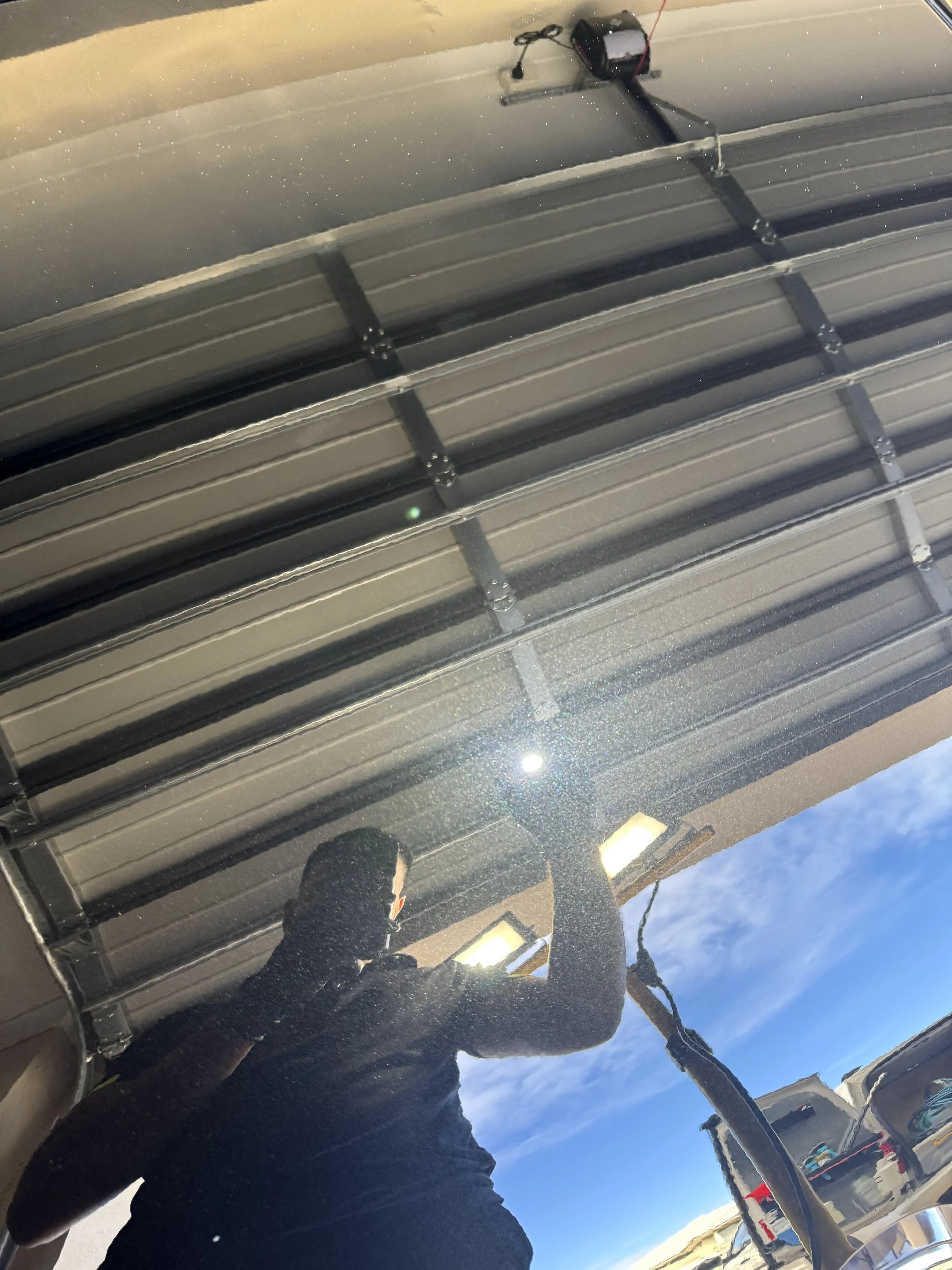 Reflective garage door with a person taking a photo, visible in the reflection, showing blue sky and clouds outside.