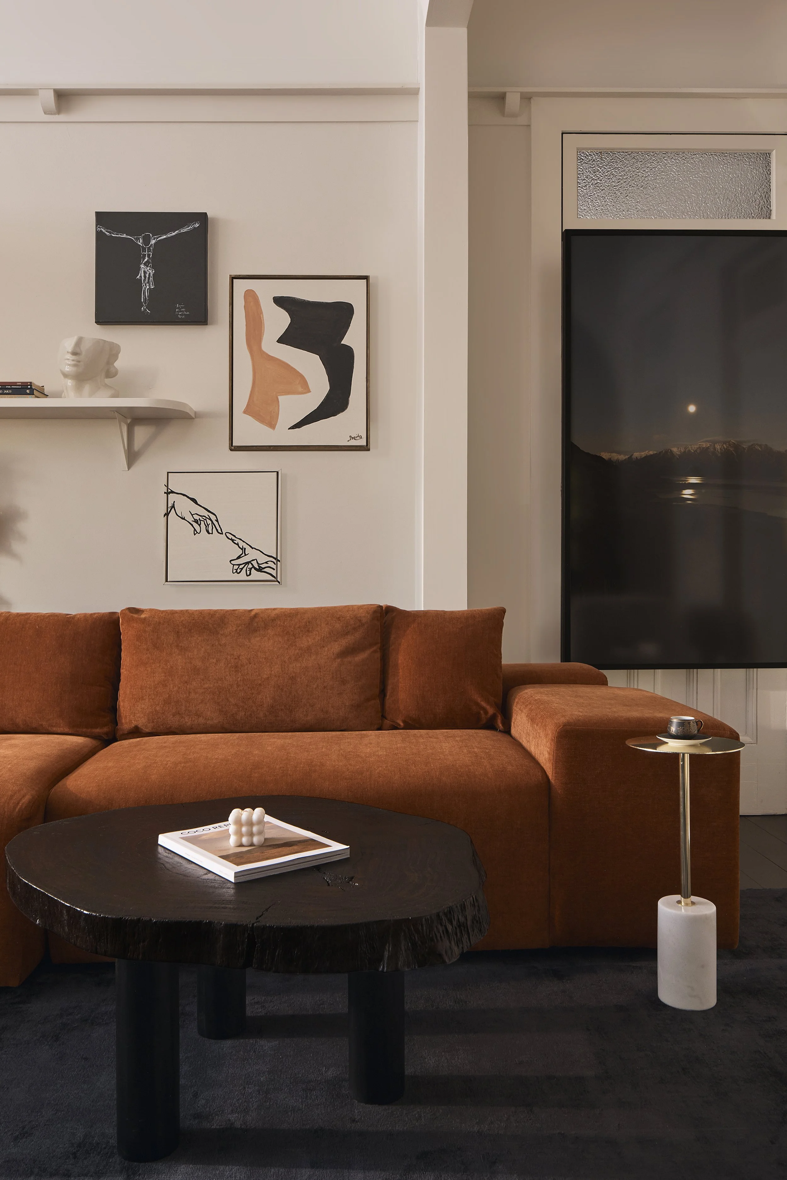 Modern Sydney home renovation blending heritage architectural details with contemporary interiors, featuring a rust-coloured sofa, timber coffee table, decorative wall mouldings and curated artwork – Sydney City Renovations.