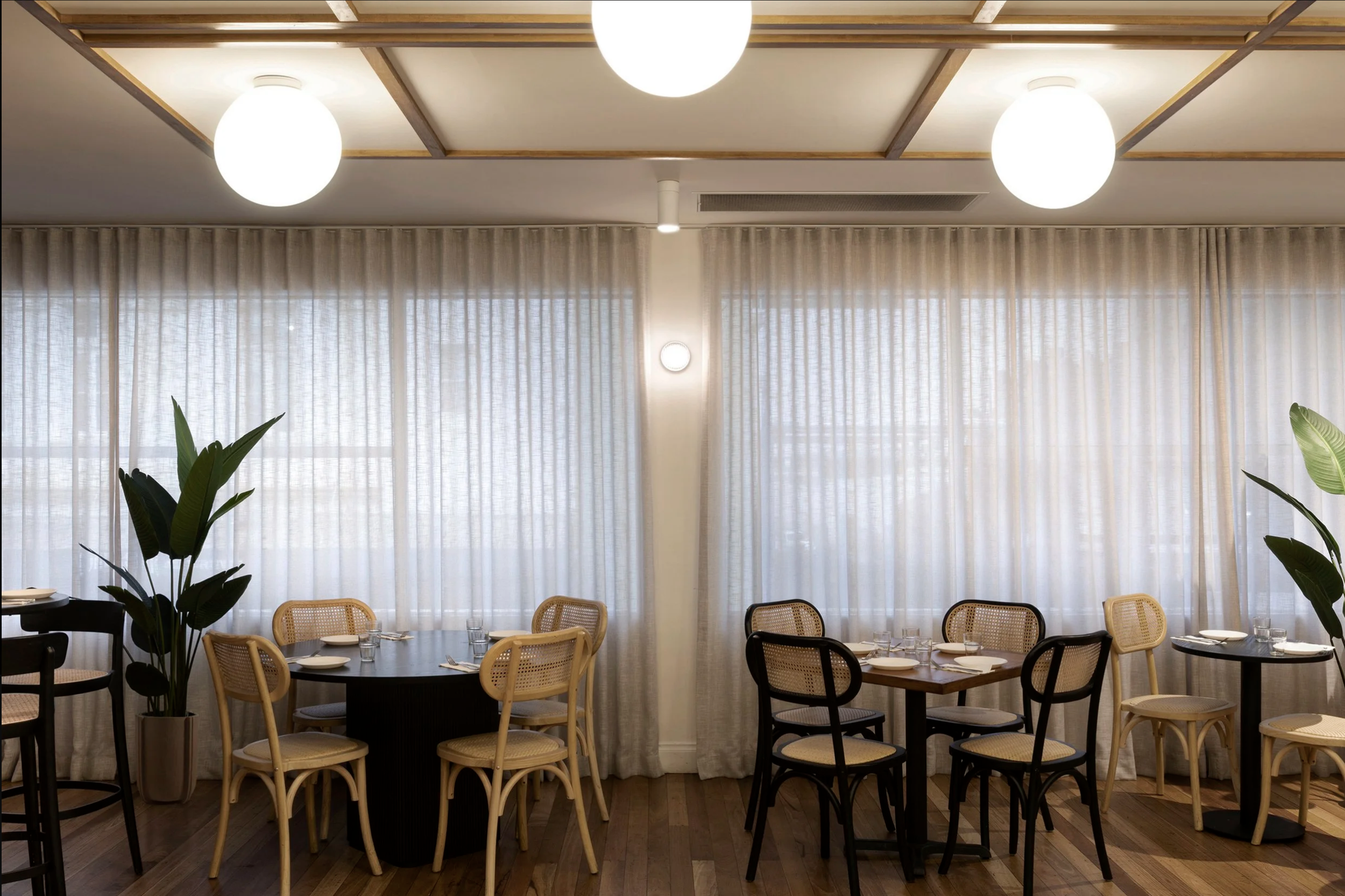 Sydney City Renovations commercial restaurant fit-out featuring timber flooring, decorative globe ceiling lights, custom floral upholstered banquette seating, natural cane dining chairs and contemporary buffet stations. 