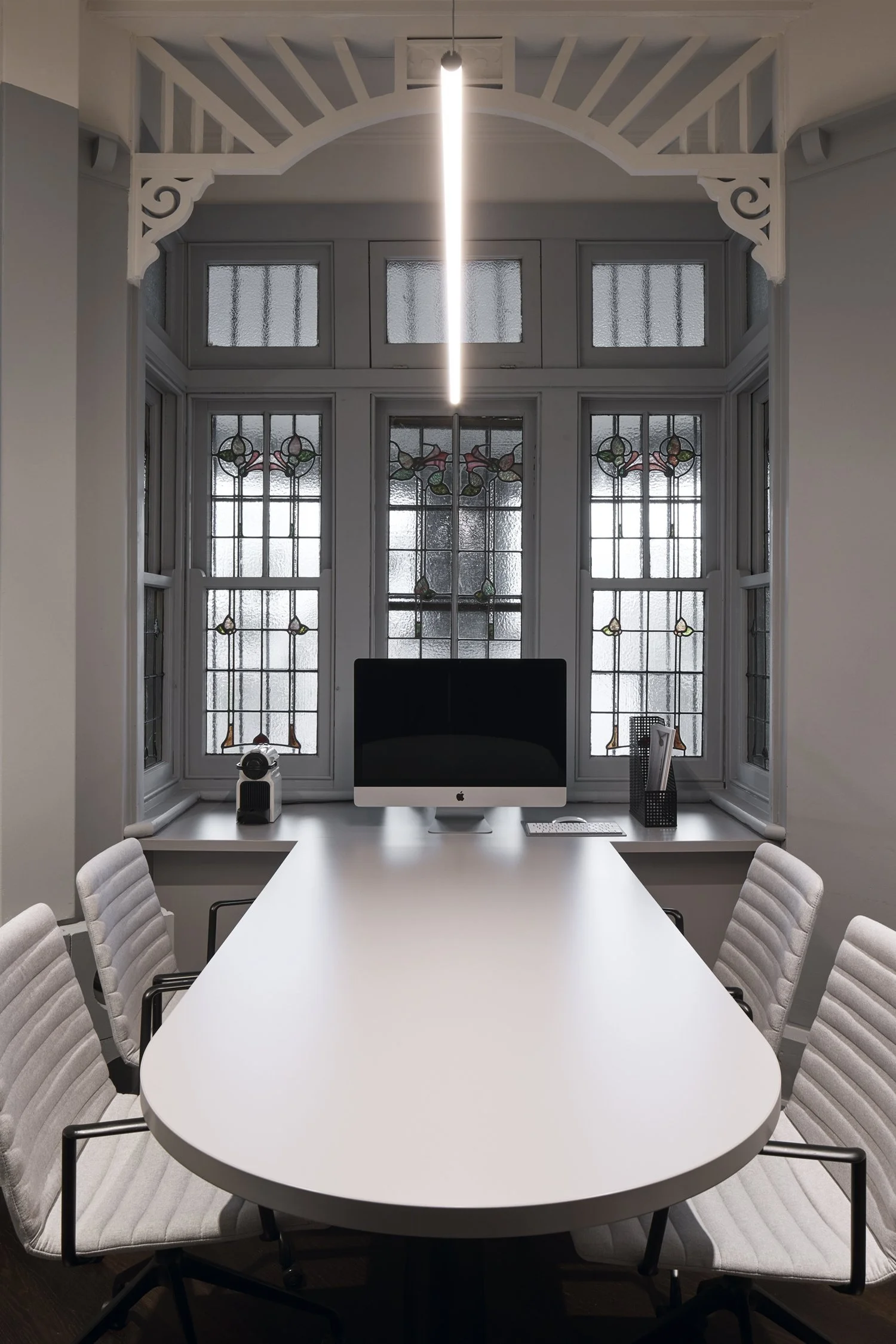 Sydney City Renovations heritage home office renovation featuring original stained-glass bay windows, decorative Federation timber detailing, a contemporary custom desk, upholstered office chairs and minimalist pendant lighting.