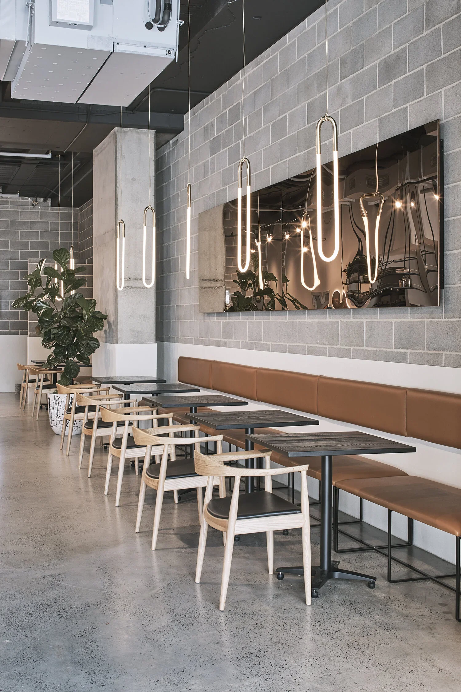 Black Seed Eatery Parramatta commercial café fit-out featuring grey brick walls, polished concrete flooring, custom tan leather banquette seating, timber chairs, contemporary pendant lighting and feature mirrors – Sydney City Renovations.