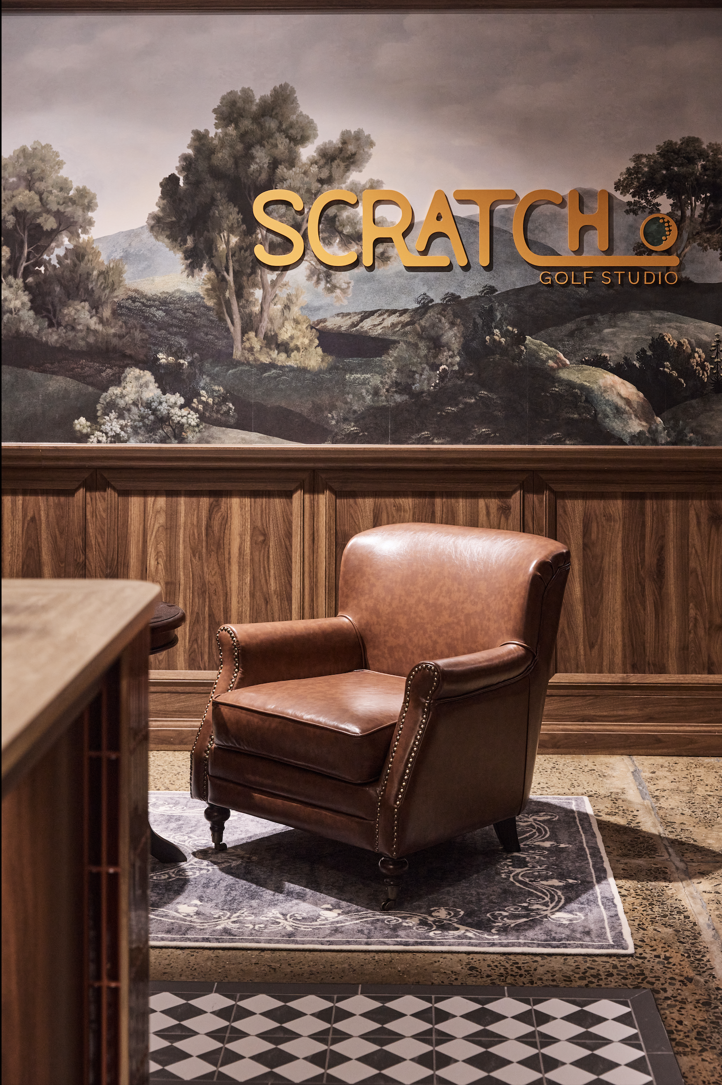 Scratch Golf Studio Marrickville commercial fit-out featuring custom golf-themed wall graphics, illuminated signage, decorative timber wall panelling, vintage leather lounge seating and geometric floor tiles – Sydney City Renovations.