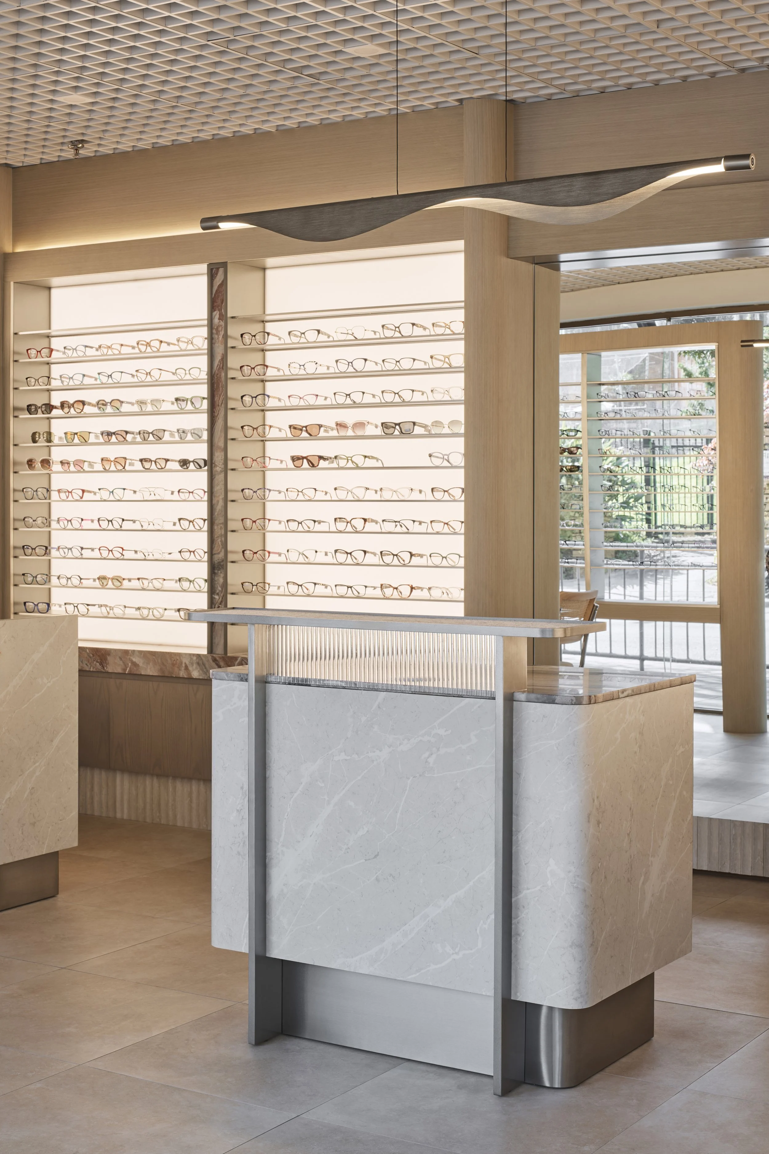 A modern shop with glasses display on illuminated shelves and a sleek curved chandelier hanging from the ceiling.