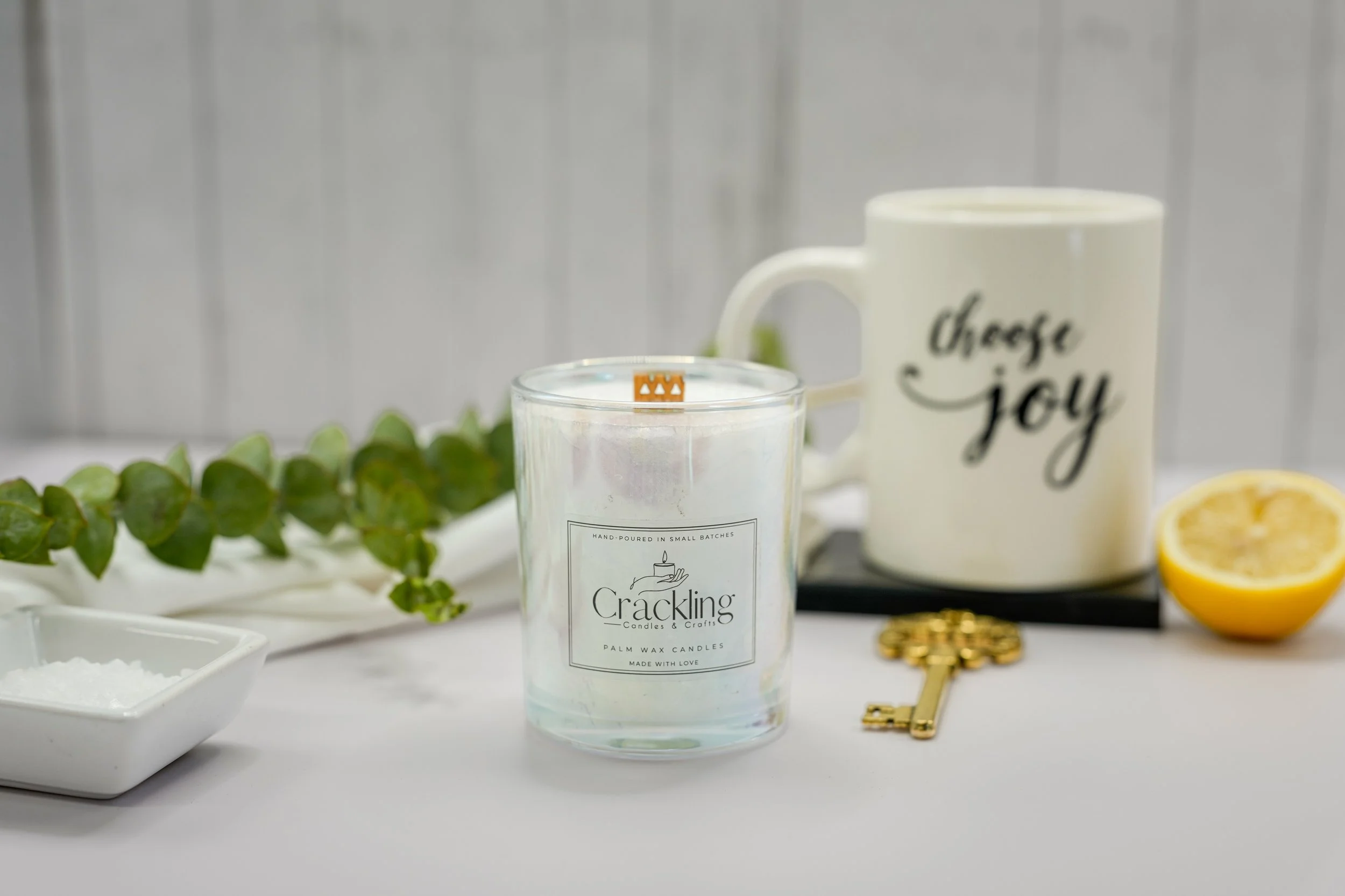 Hand-poured Blood Orange candle with a wooden wick, styled with fresh greenery, a Choose Joy mug, and a decorative brass key.