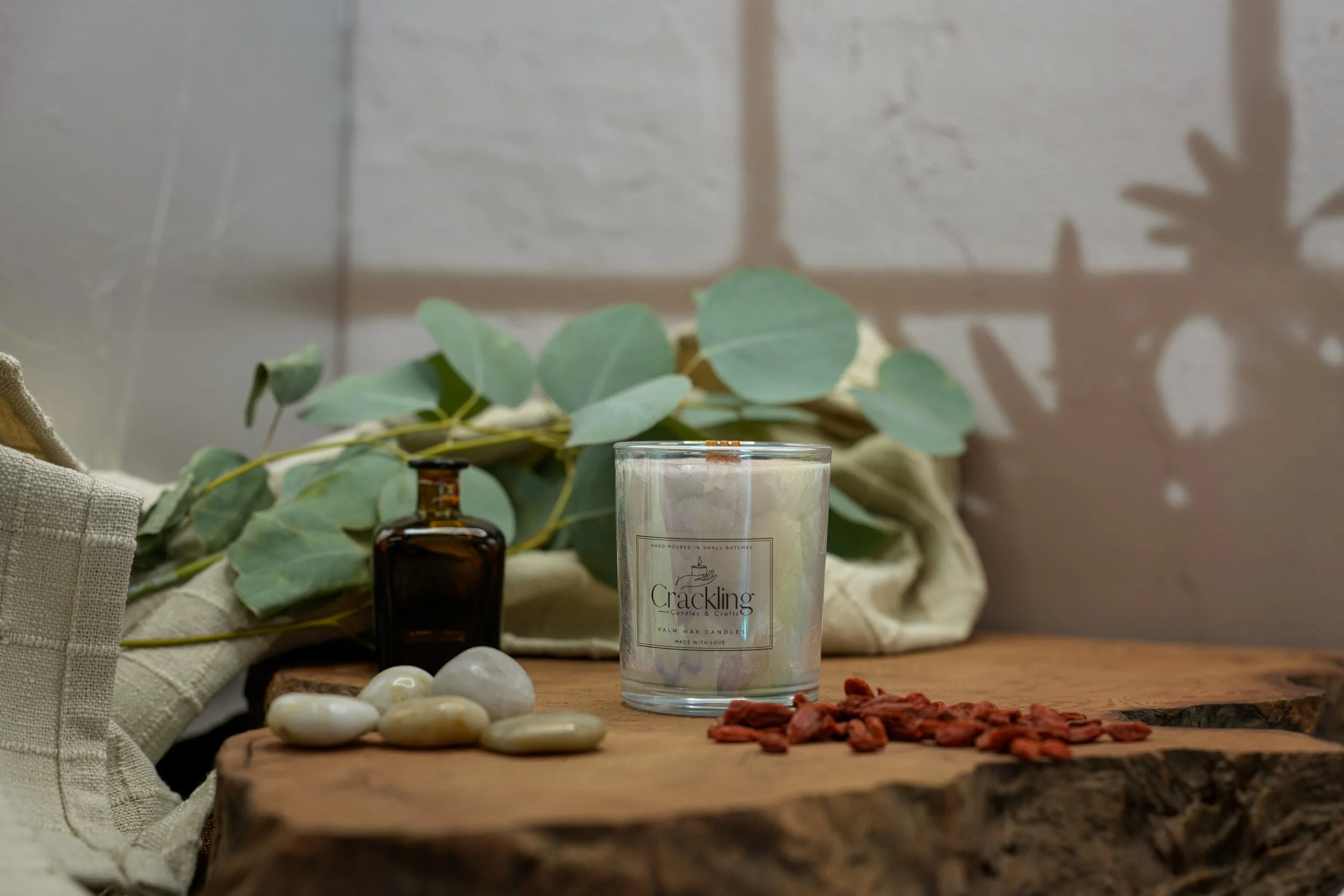 Closer front view of a 6 oz Tobacco & Oud palm wax candle with a wooden wick, eucalyptus, stones, and an amber bottle