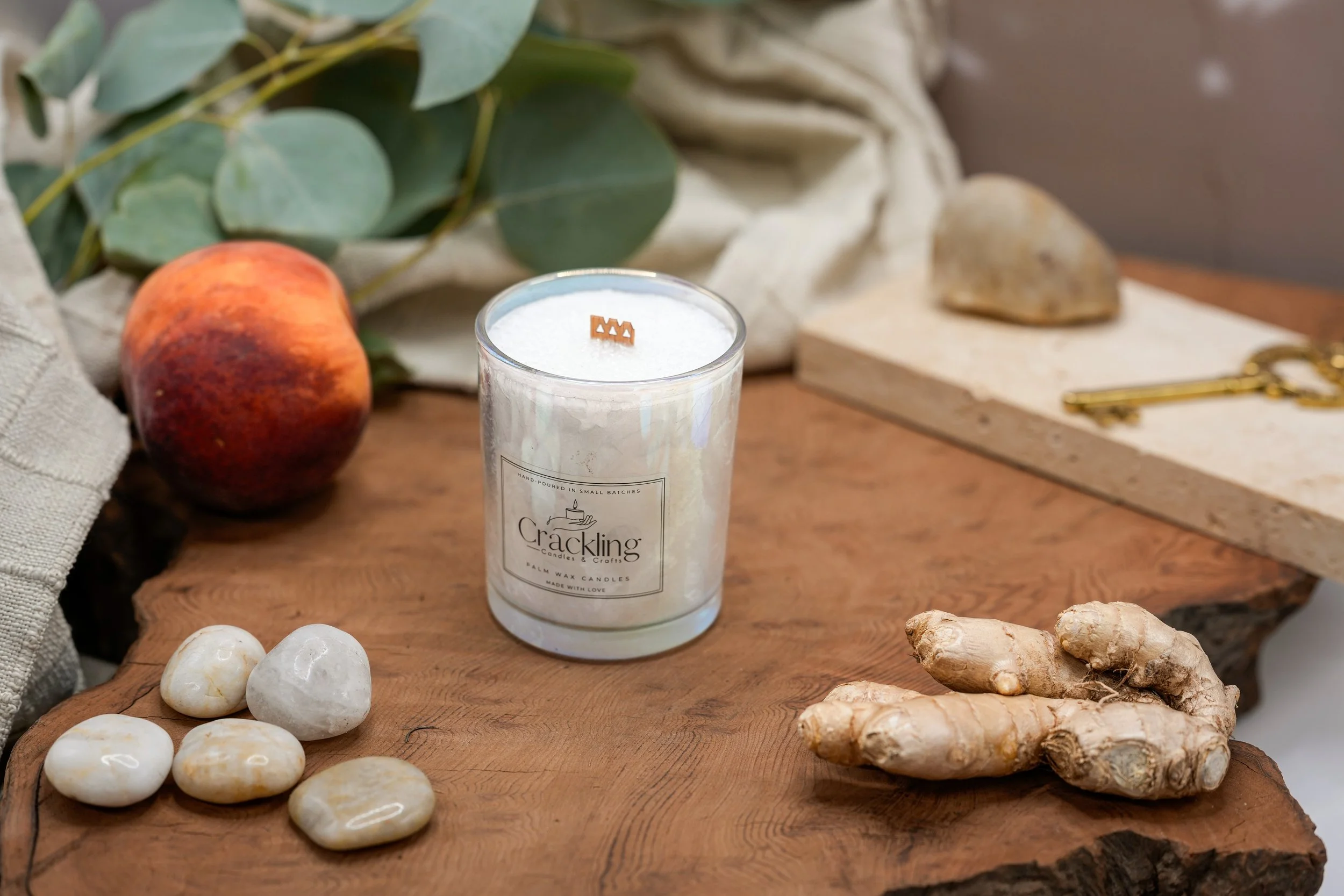 Gingered Peach candle in a glass jar on a wooden surface with a peach, ginger, and smooth stones.