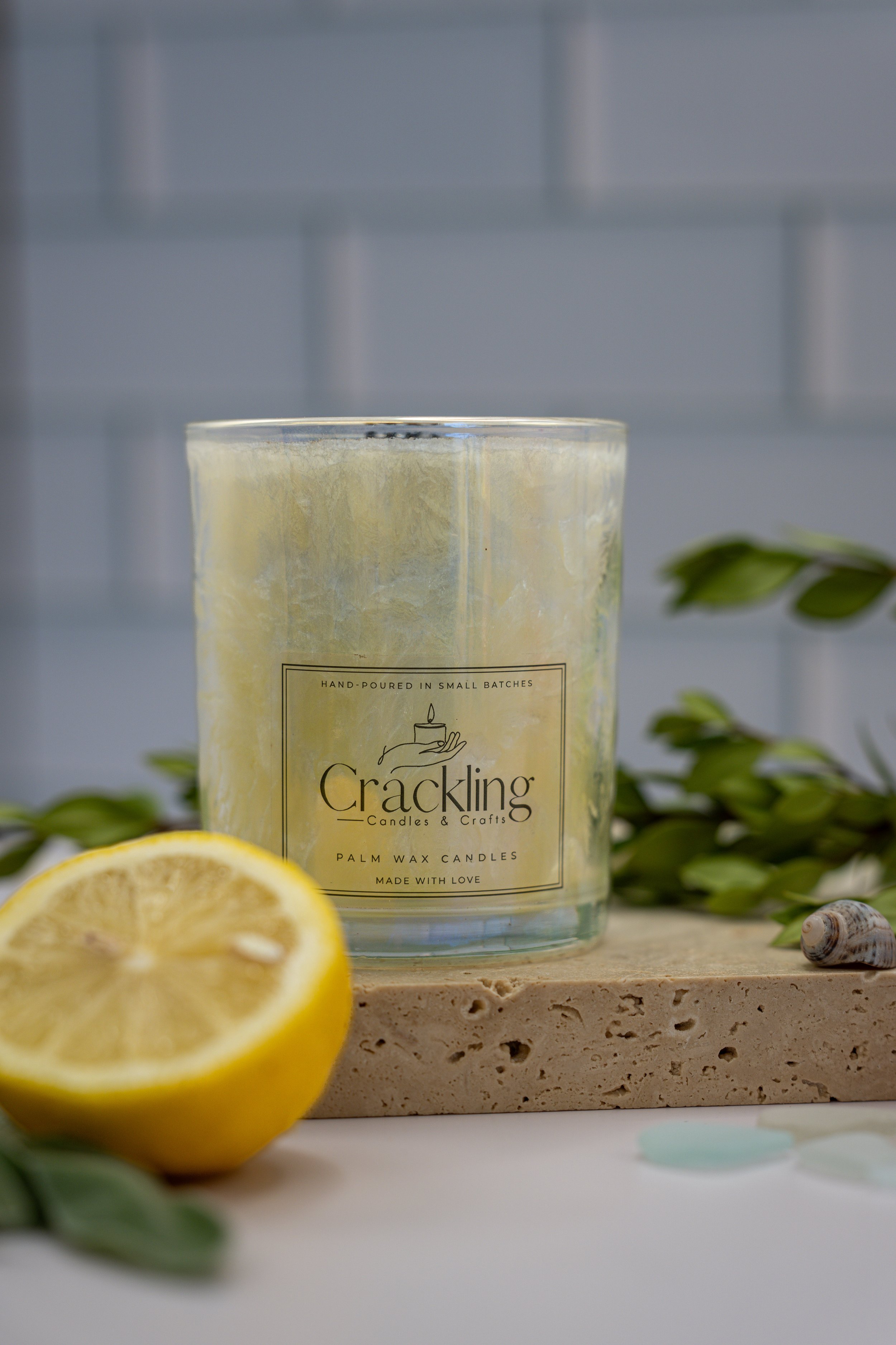 Close view of Sage & Citrus palm wax candle showing its glass jar, wooden wick, and label beside a lemon half.