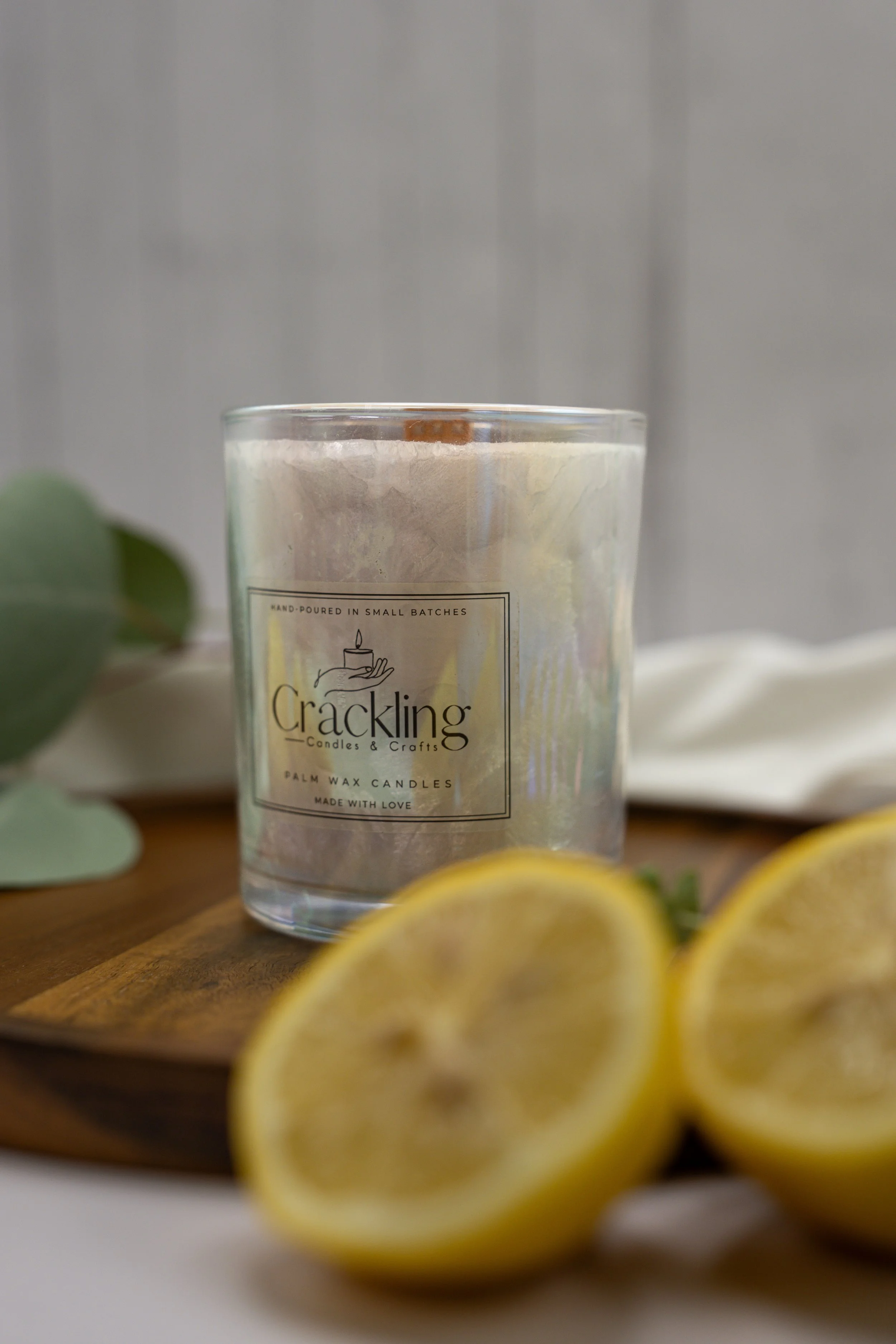 Lemon palm wax candle in a clear glass jar on a wooden board, with sliced lemons in the foreground.
