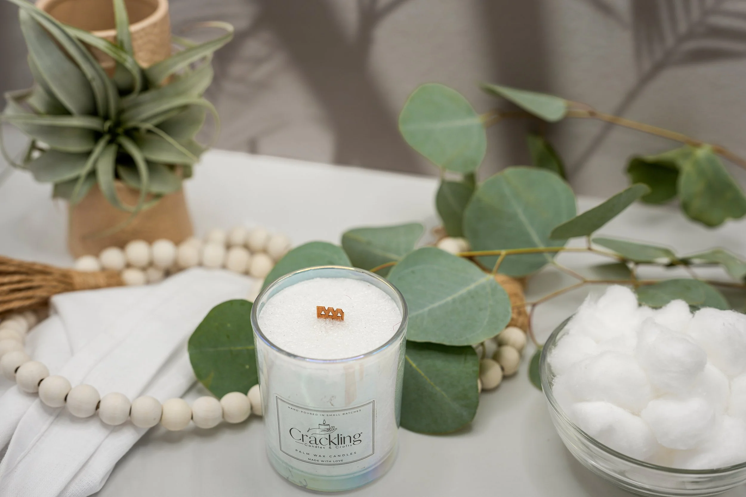 Top view of a Baby Powder palm wax candle with a wooden wick, surrounded by eucalyptus leaves, cotton, and natural beads.