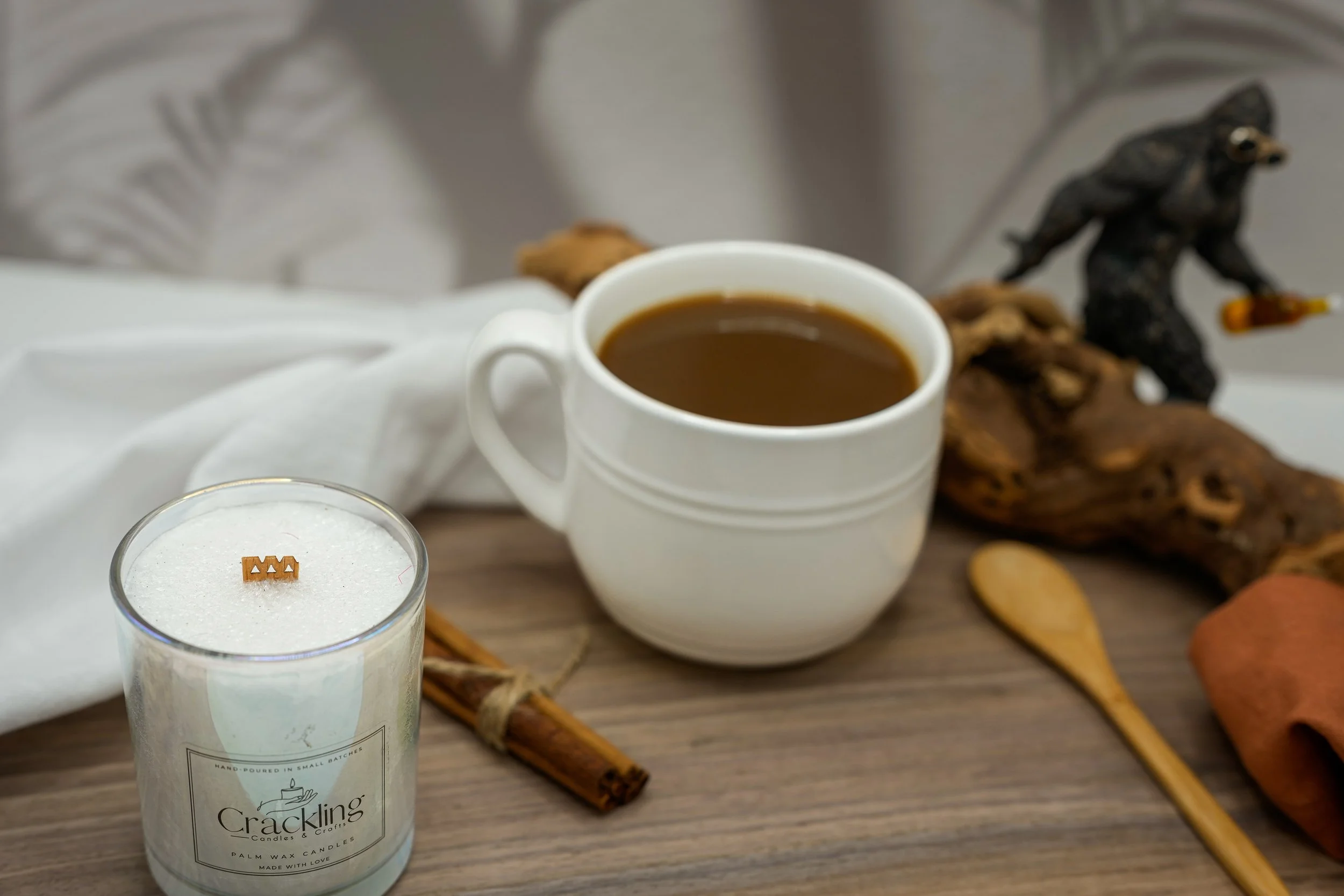 Hand-poured Coffee candle beside a white mug of coffee with cinnamon sticks and coffee beans.