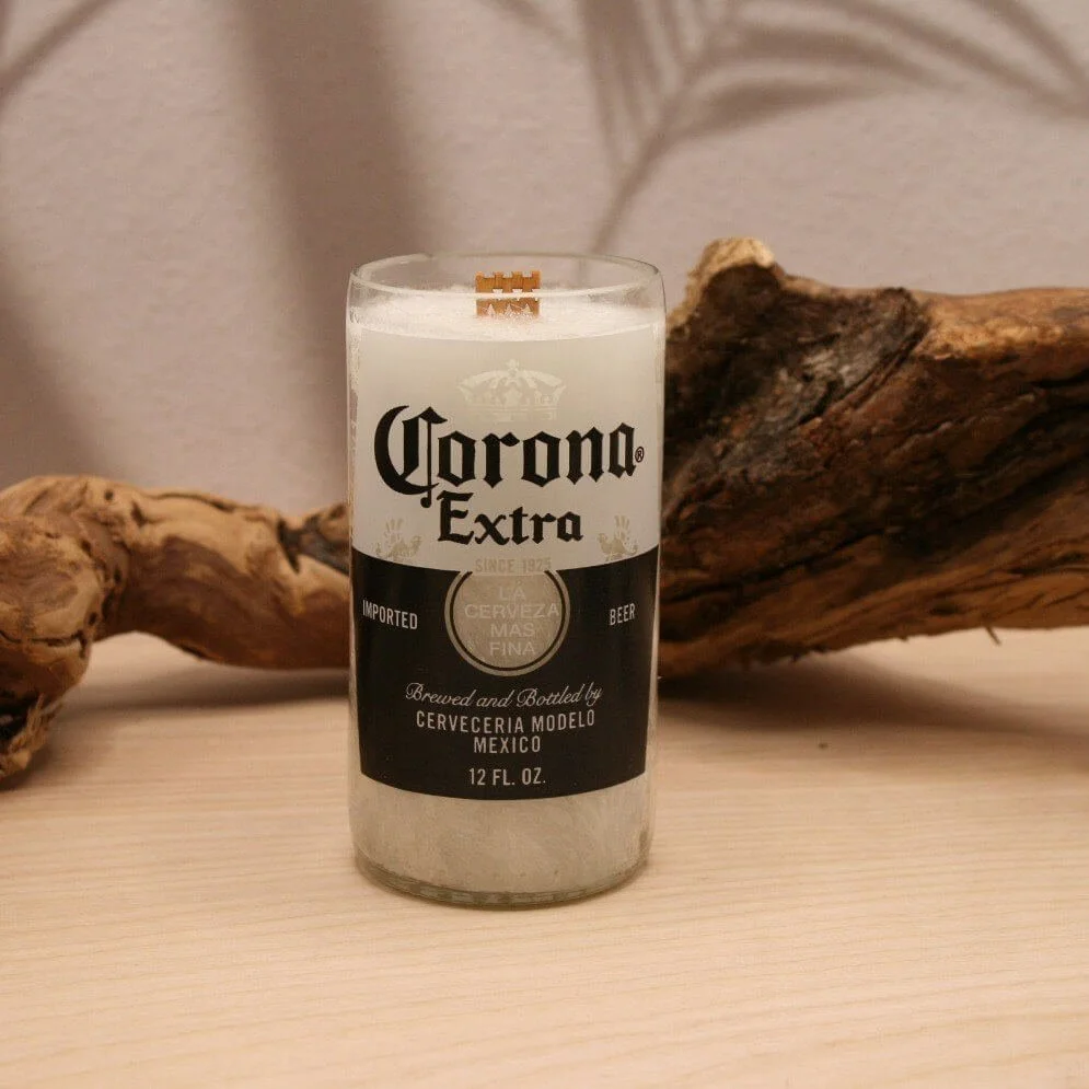 A candle with a Corona Extra beer label on a wooden surface, with driftwood in the background.