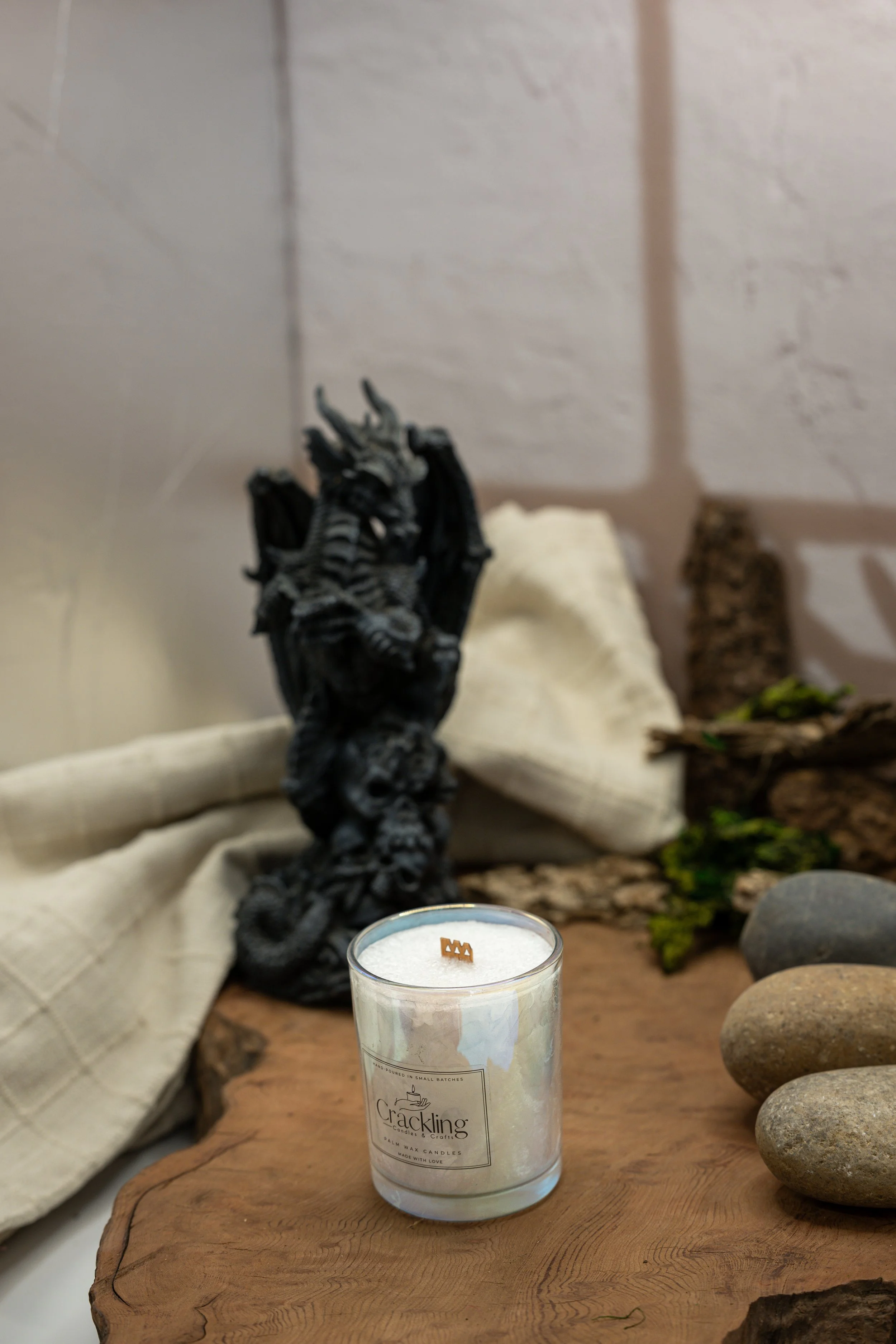 Dragon’s Blood candle in a clear glass jar beside a black dragon figurine, styled with natural wood, moss, and stones.