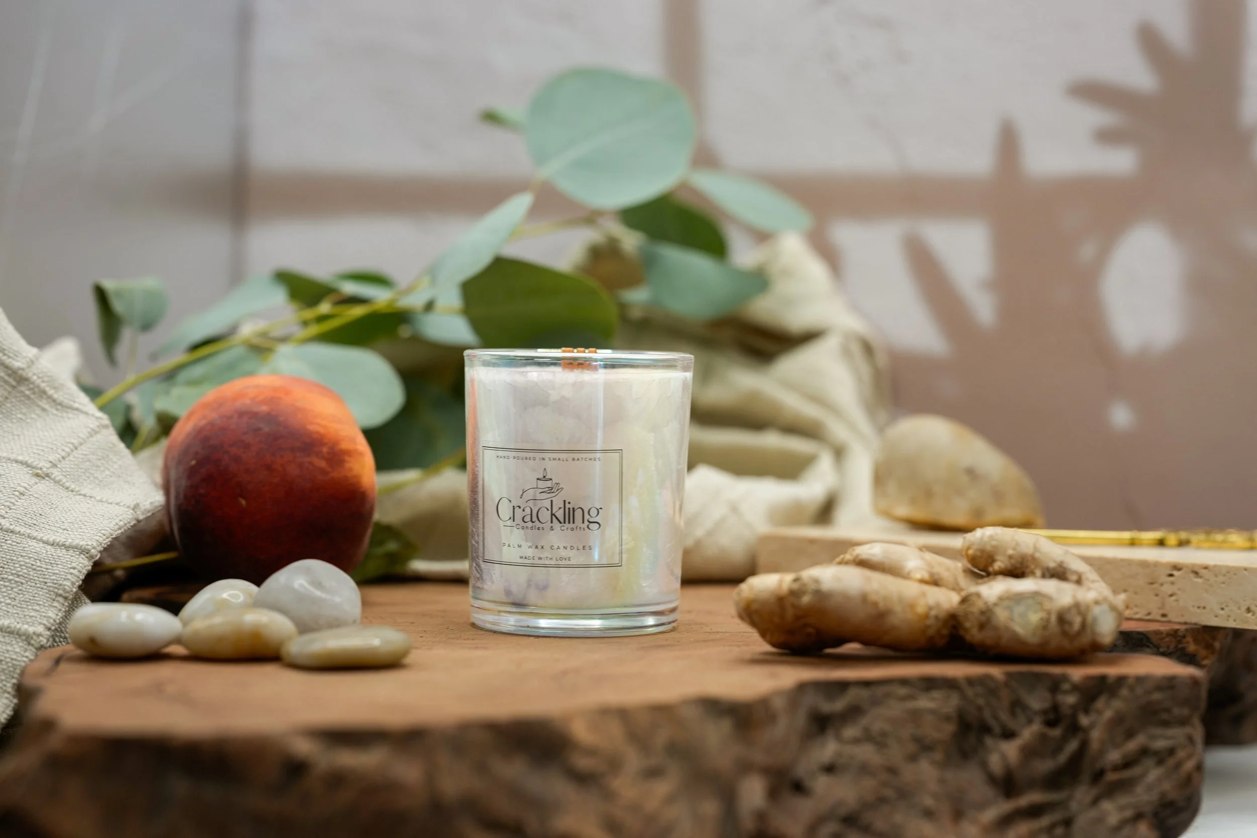 Front view of the Gingered Peach candle styled with a peach, ginger, greenery, and natural wood.