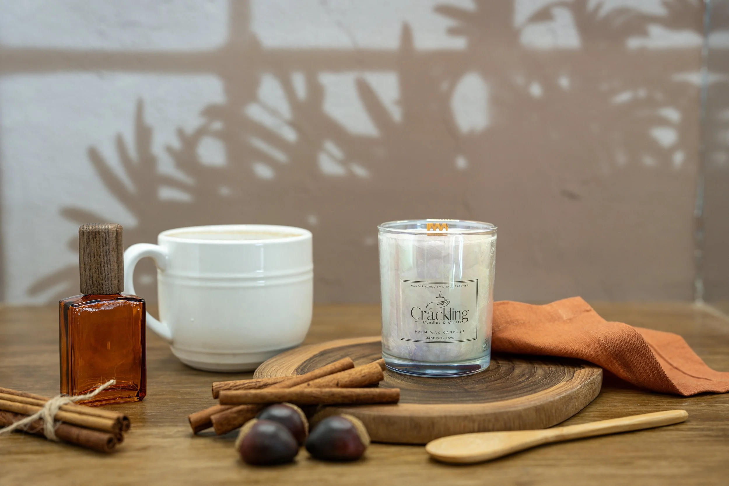 6 oz Hazelnut Cappuccino candle beside a coffee cup, cinnamon sticks, and hazelnuts on a wooden board