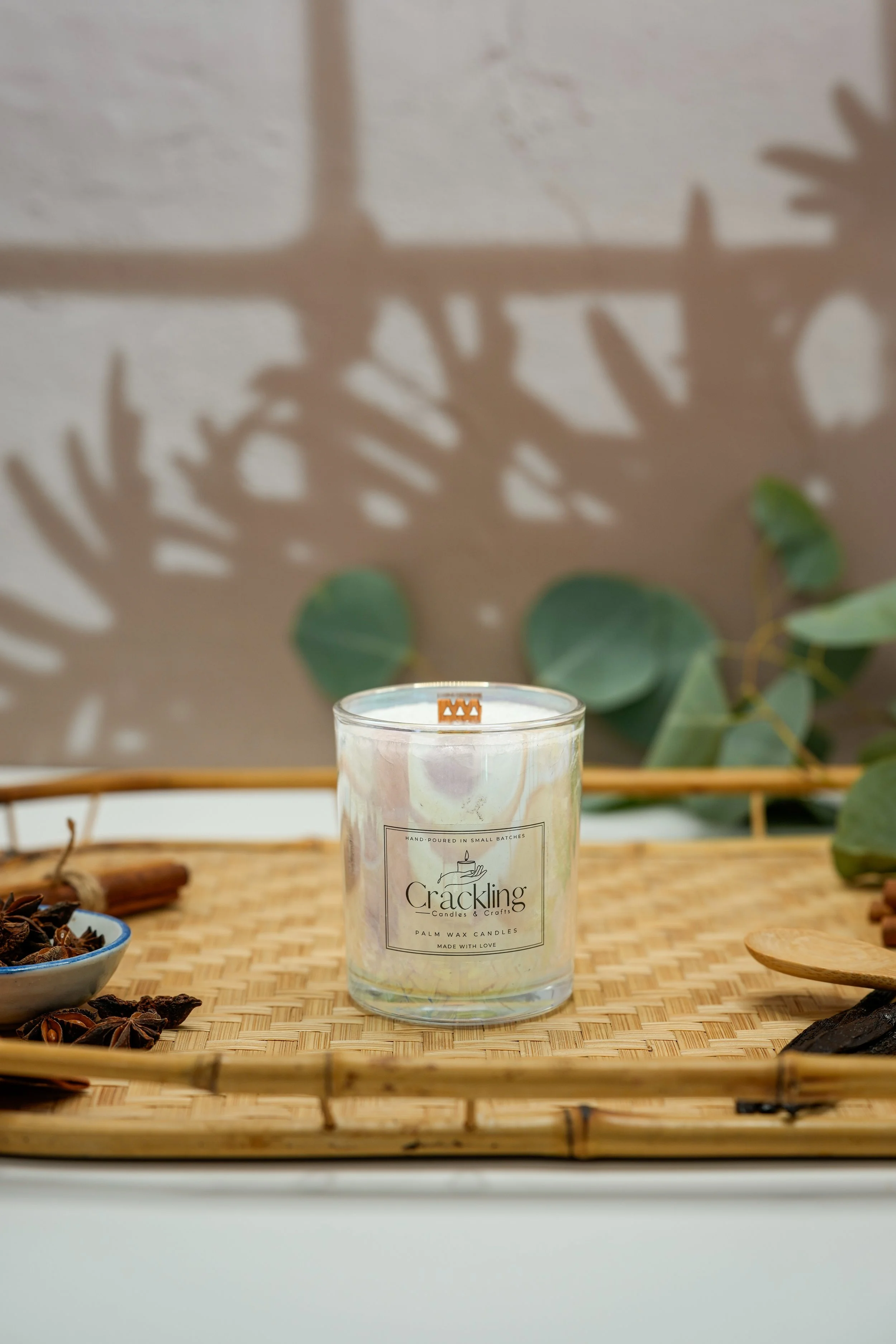 Clove candle displayed on a natural wood tray with eucalyptus leaves, whole cloves, and warm neutral decor.