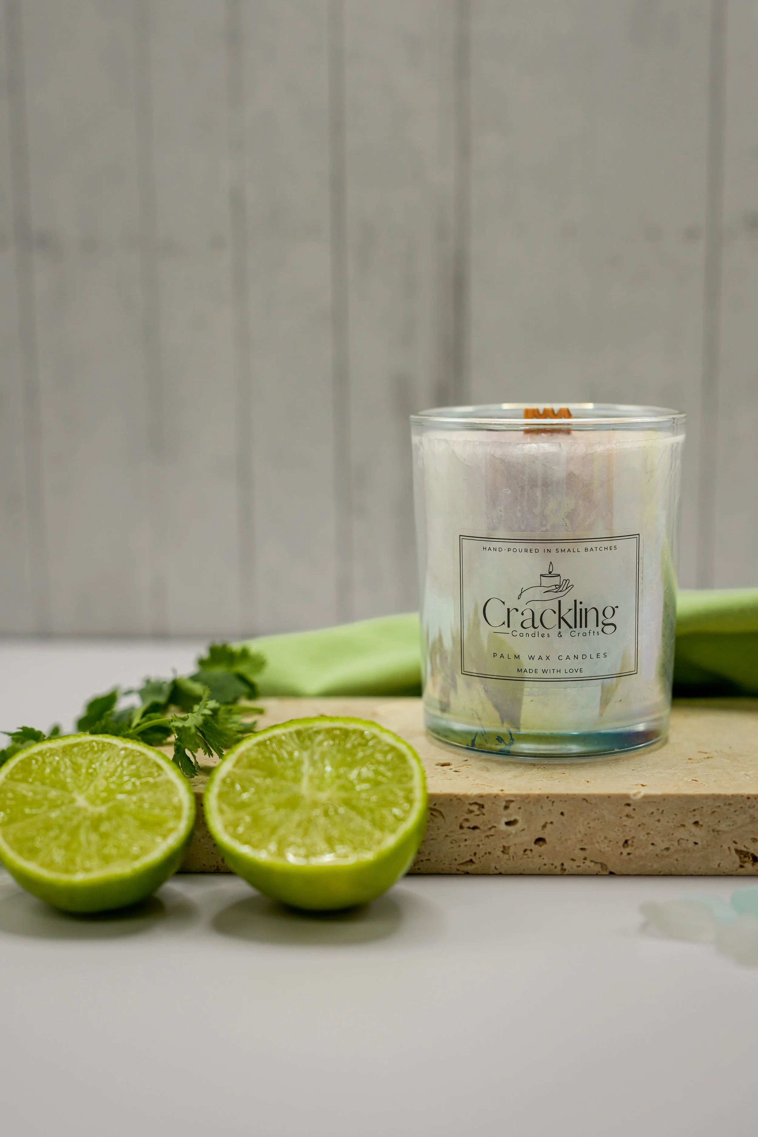 Lime Cilantro palm wax candle in a clear glass jar, styled with two lime halves, cilantro, and green fabric.