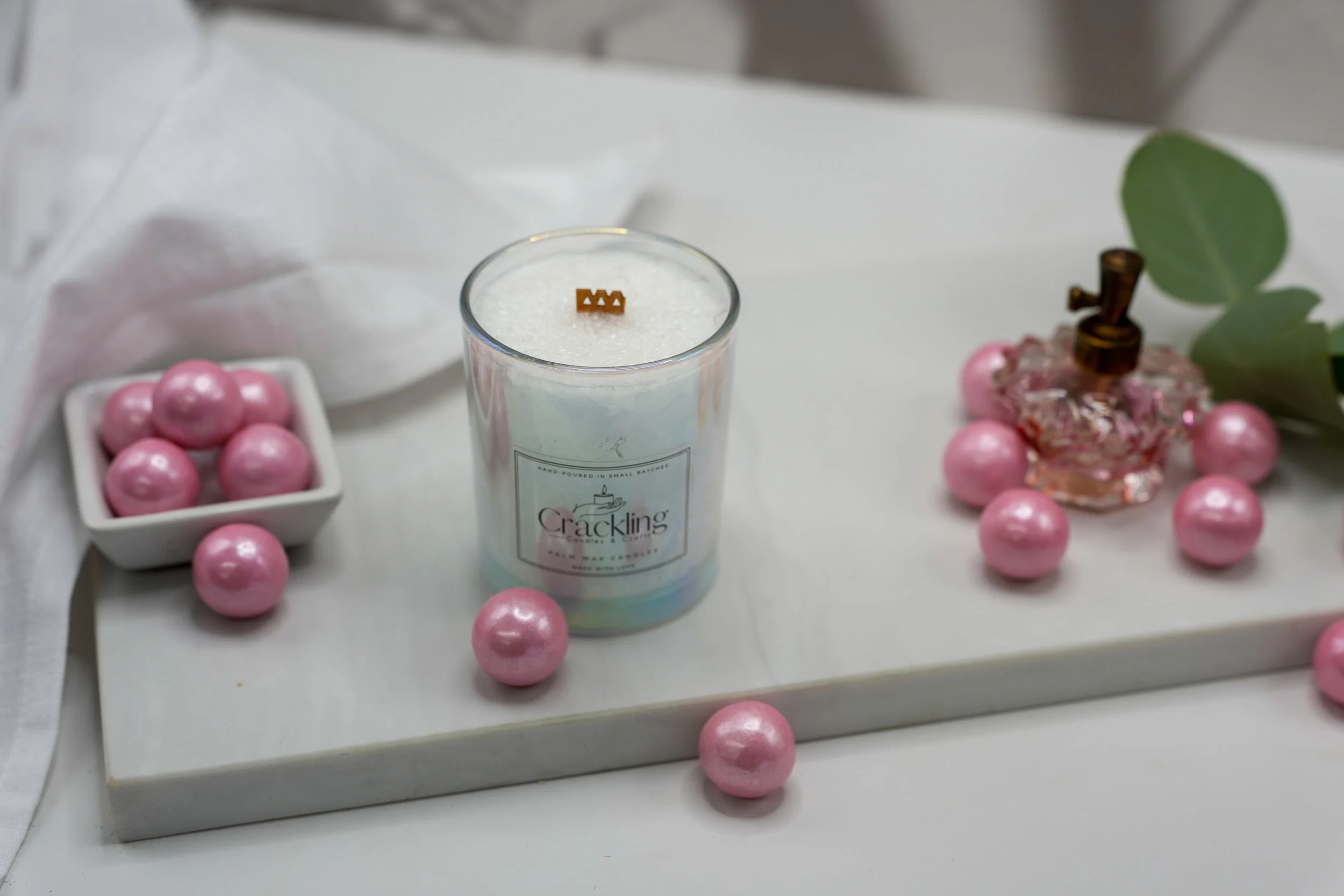 Top view of a Bubble Gum palm wax candle with a wooden wick, surrounded by glossy pink gumballs on a white surface.