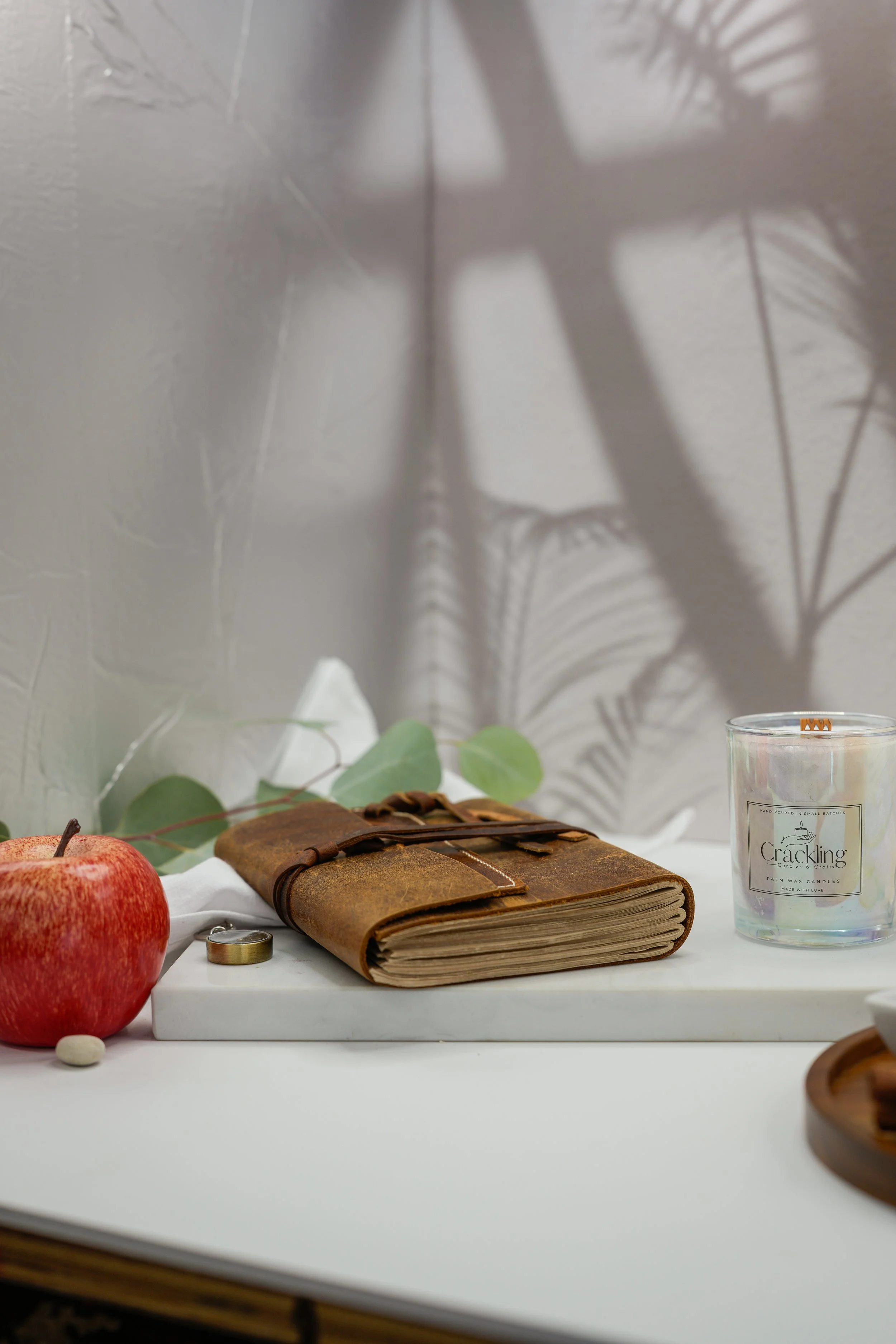 Hand-poured Apple Jazz candle with a wooden wick, photographed with a fresh red apple, a leather journal, and greenery.
