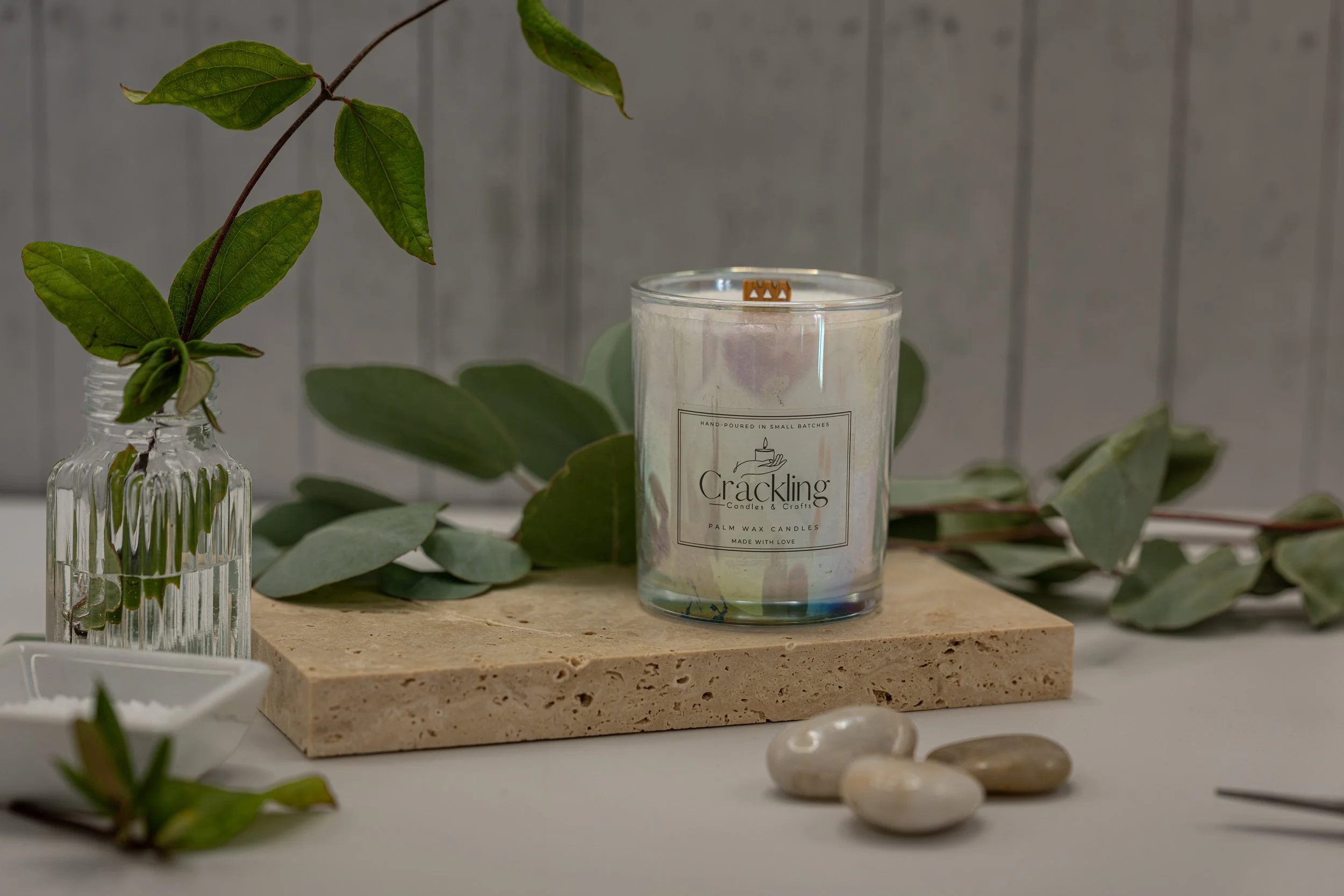 Eucalyptus & Spearmint candle in a clear glass jar on a beige stone riser, surrounded by eucalyptus leaves and smooth stones.