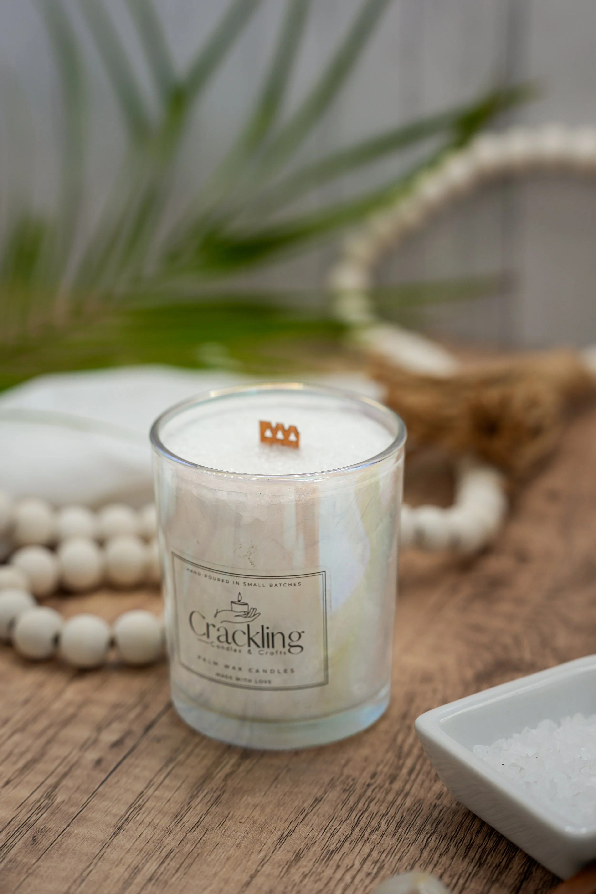Close-up of a Coconut candle with a wooden wick, styled with white beads, palm greenery, coconut, and soft neutral decor.
