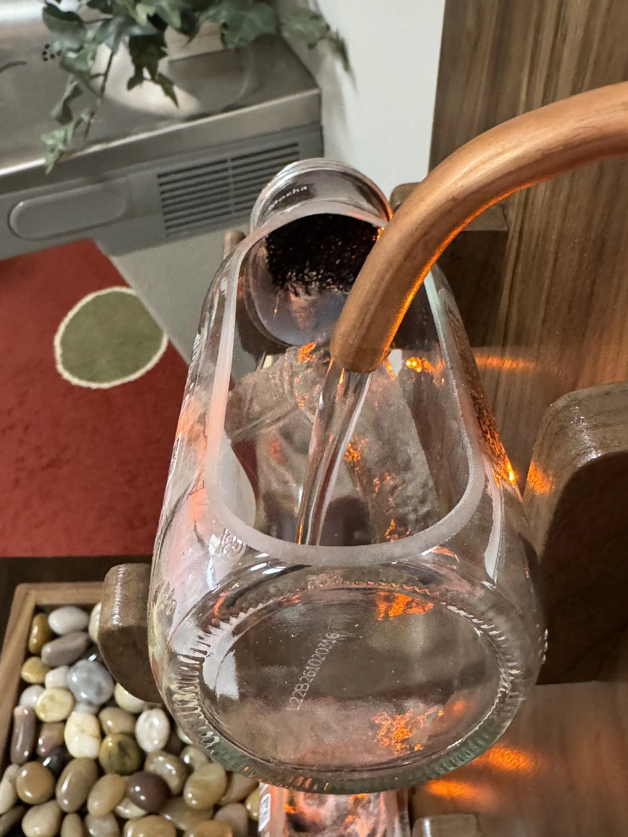 Close-up of the copper tube delivering water into an open glass bottle in the redwood Frappuccino fountain.