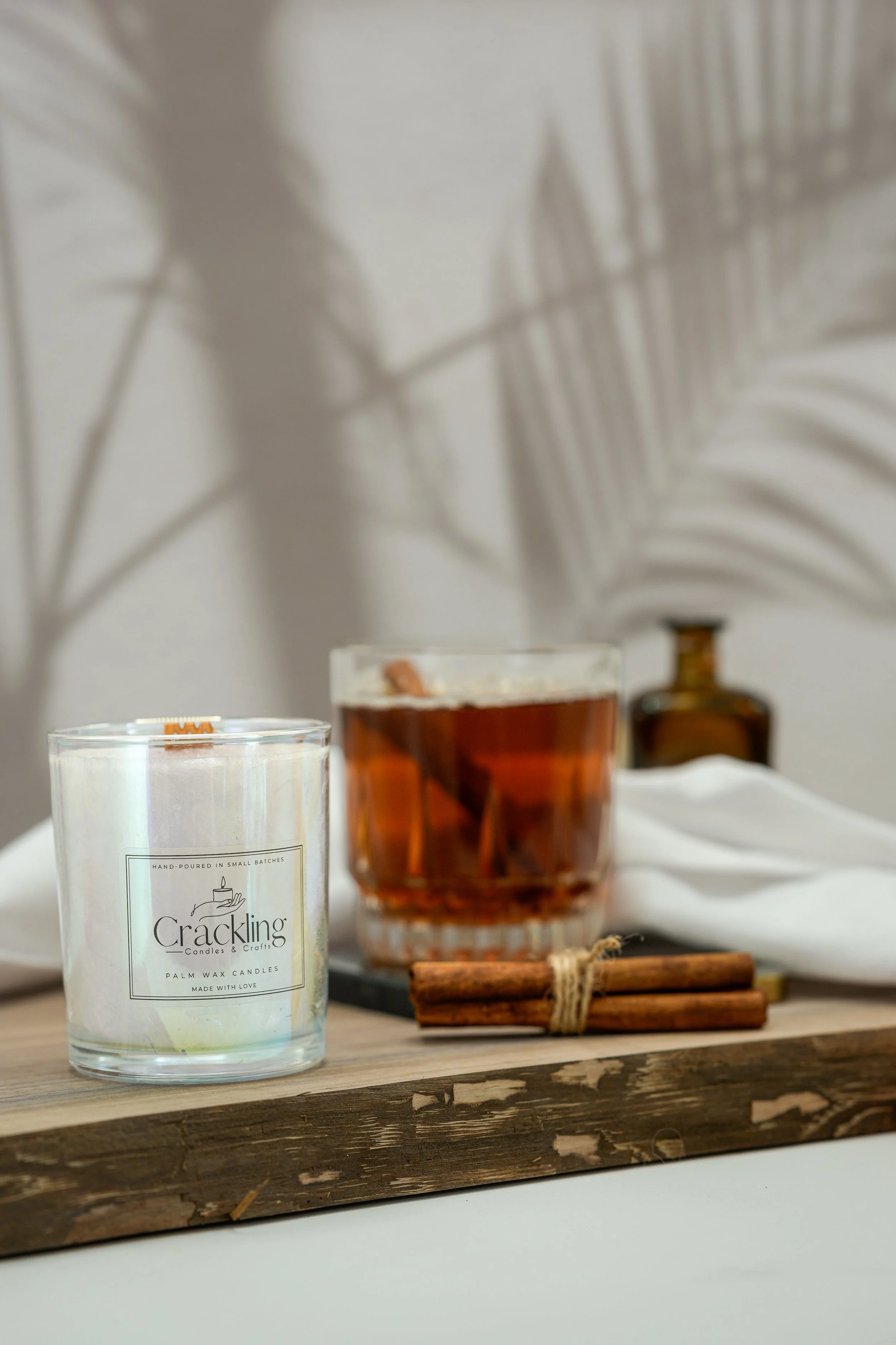 Maple Whiskey Toddy palm wax candle in a clear glass jar beside an amber drink and cinnamon sticks on a wooden board.