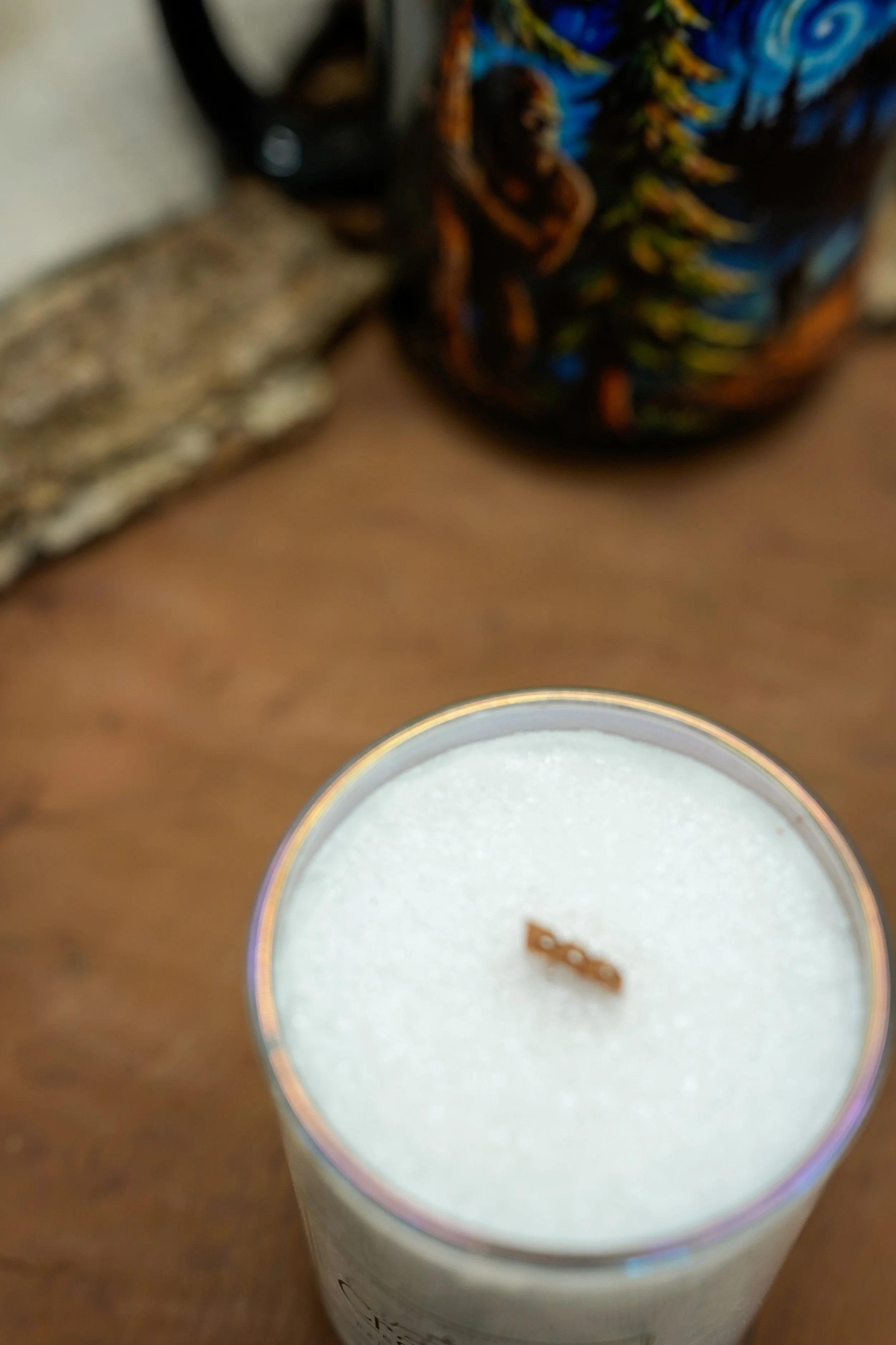 Close-up of a Caribbean Teakwood palm wax candle with a wooden wick on warm rustic wood.