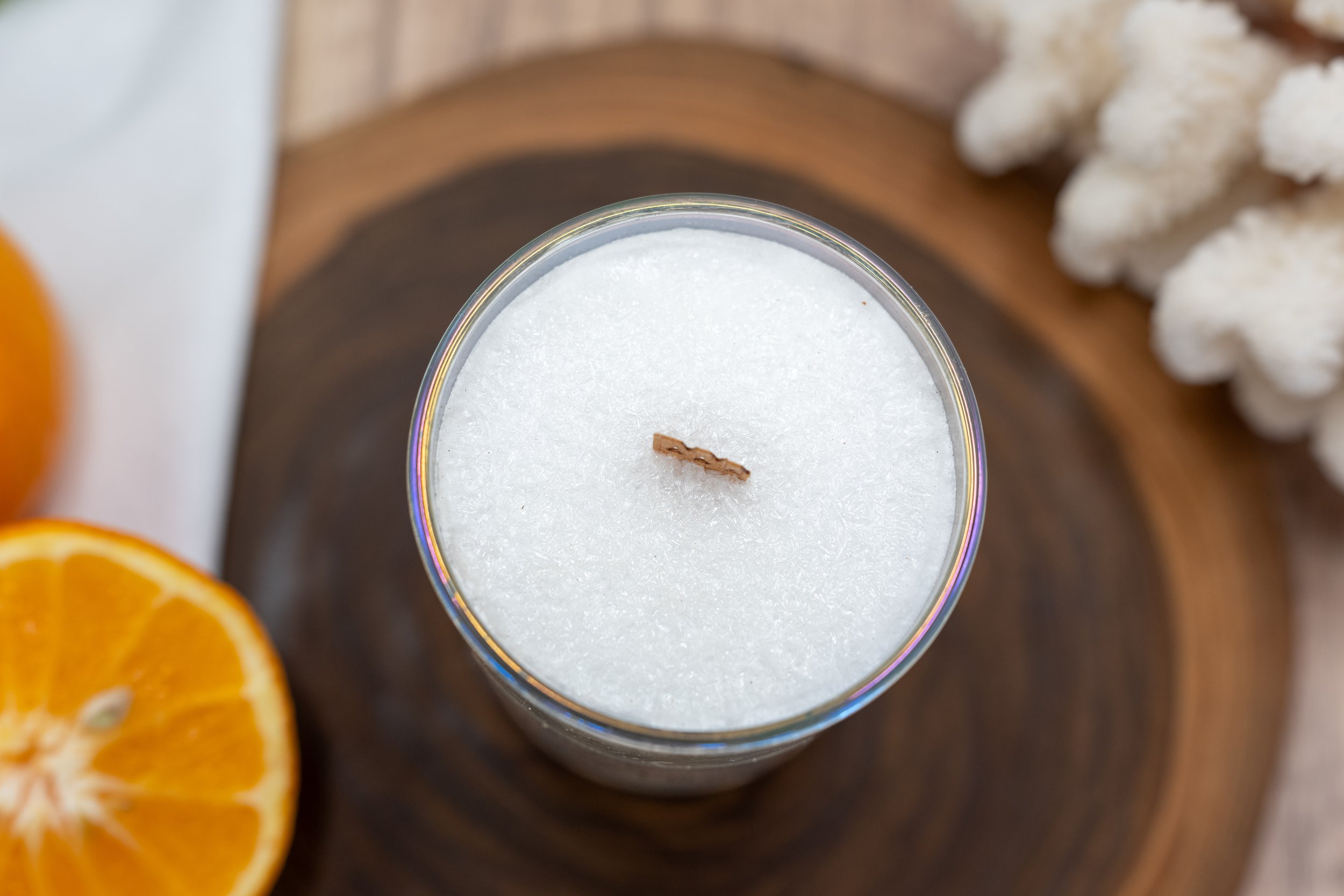 Close-up of a 6 oz Bite Me palm wax candle with a wooden wick, fresh orange, tropical greenery, and natural decor.