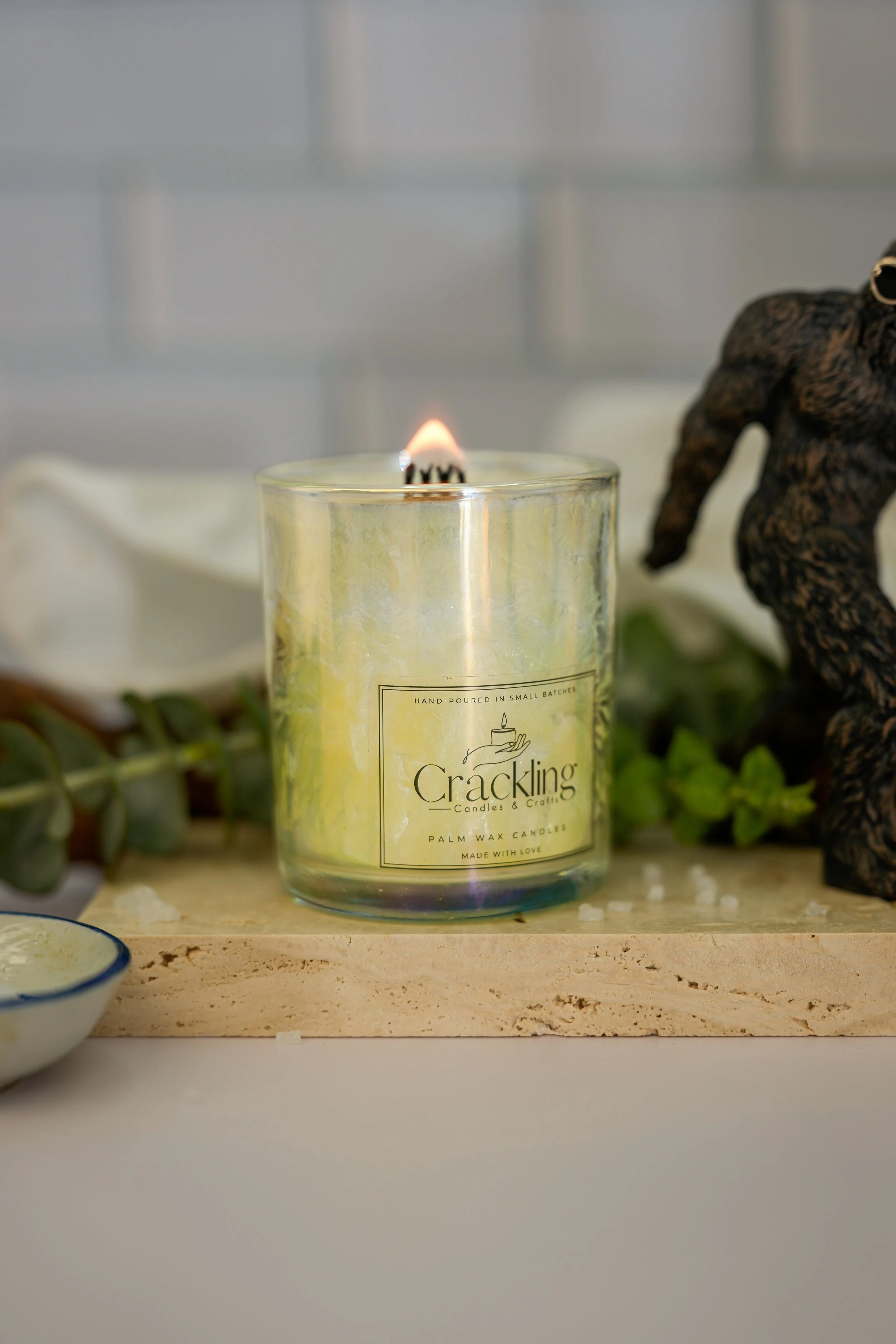 Lit White Sage & Sea Salt candle with a wooden wick and natural greenery