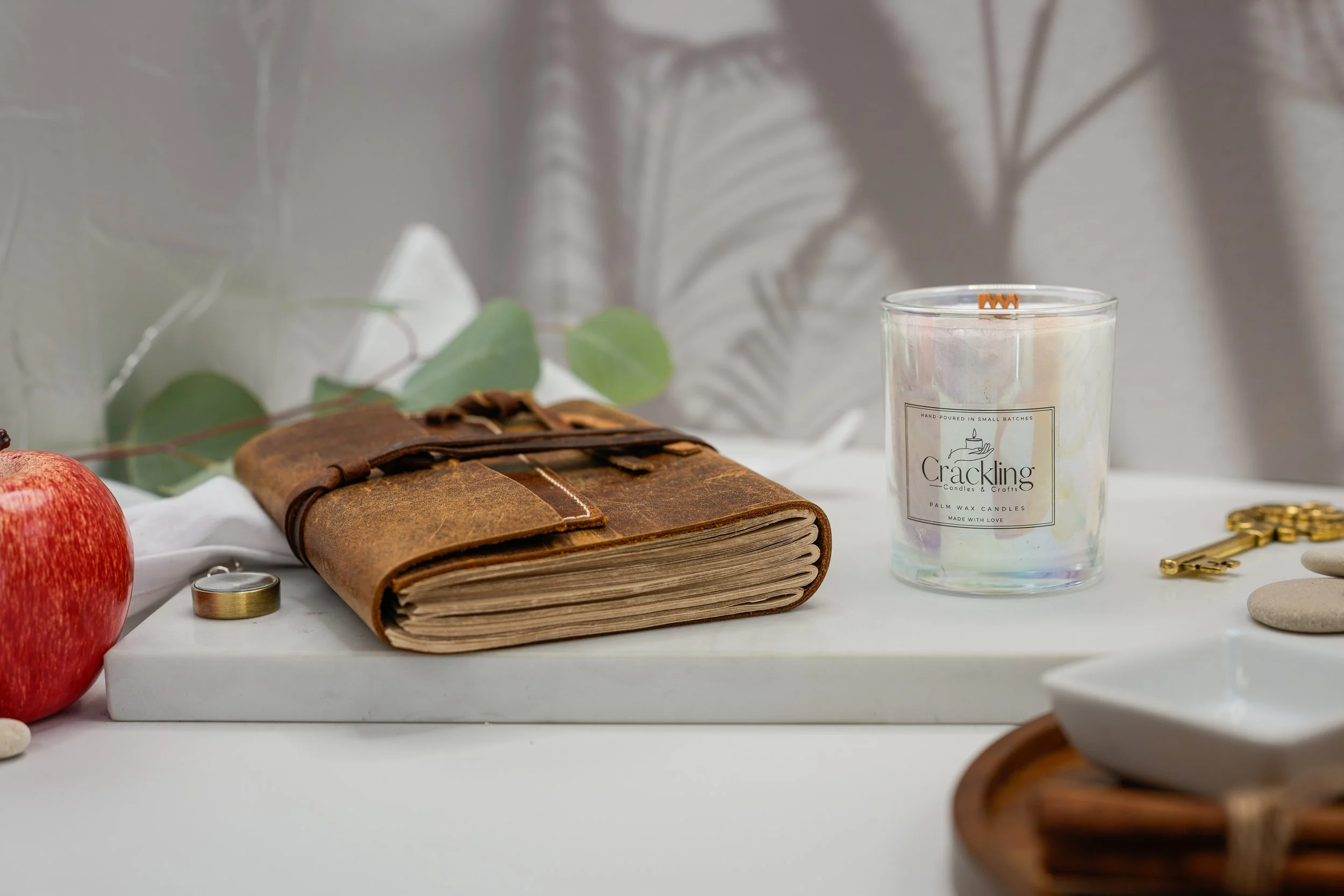 Apple Jazz candle displayed beside stacked leather journals and soft greenery in a warm neutral setting.