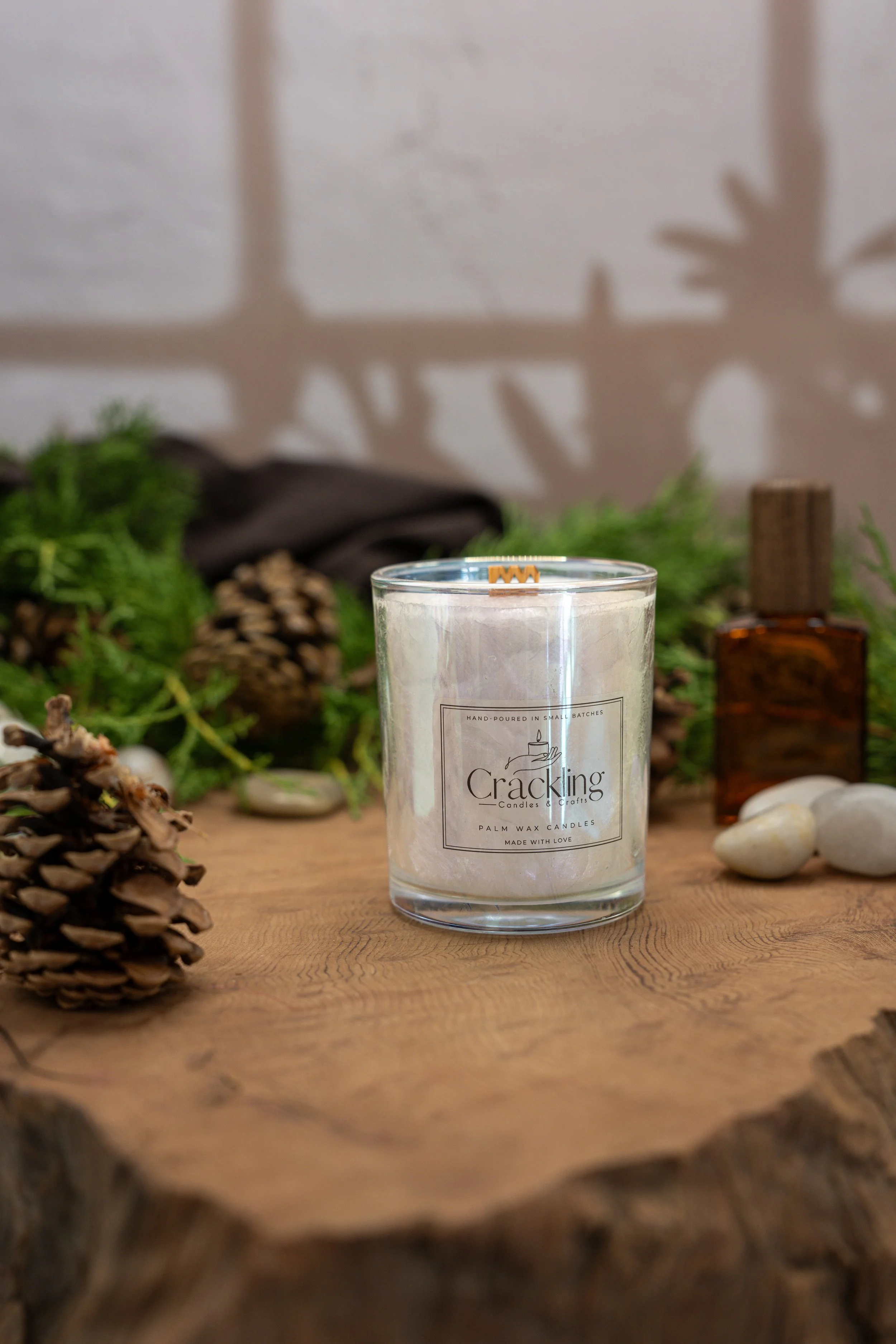Close-up of a Cedarwood and Amber candle with a wooden wick, styled with greenery, pinecones, rustic wood, and amber decor.