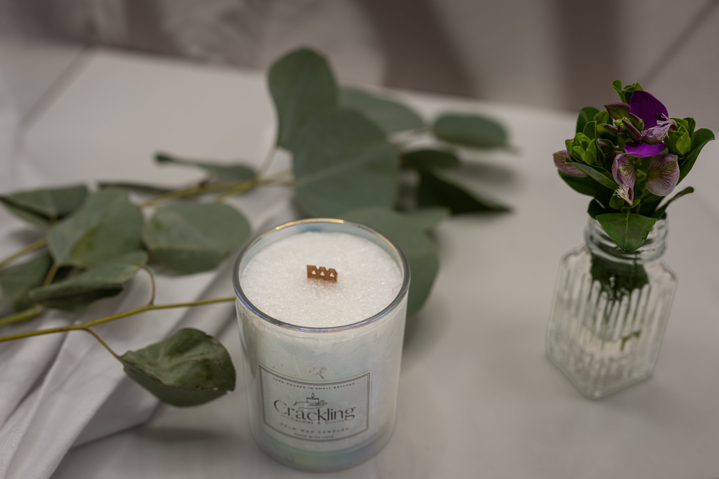 Top view of a 6 oz Sweet Pea palm wax candle with a wooden wick, styled with fresh eucalyptus on a soft neutral background.