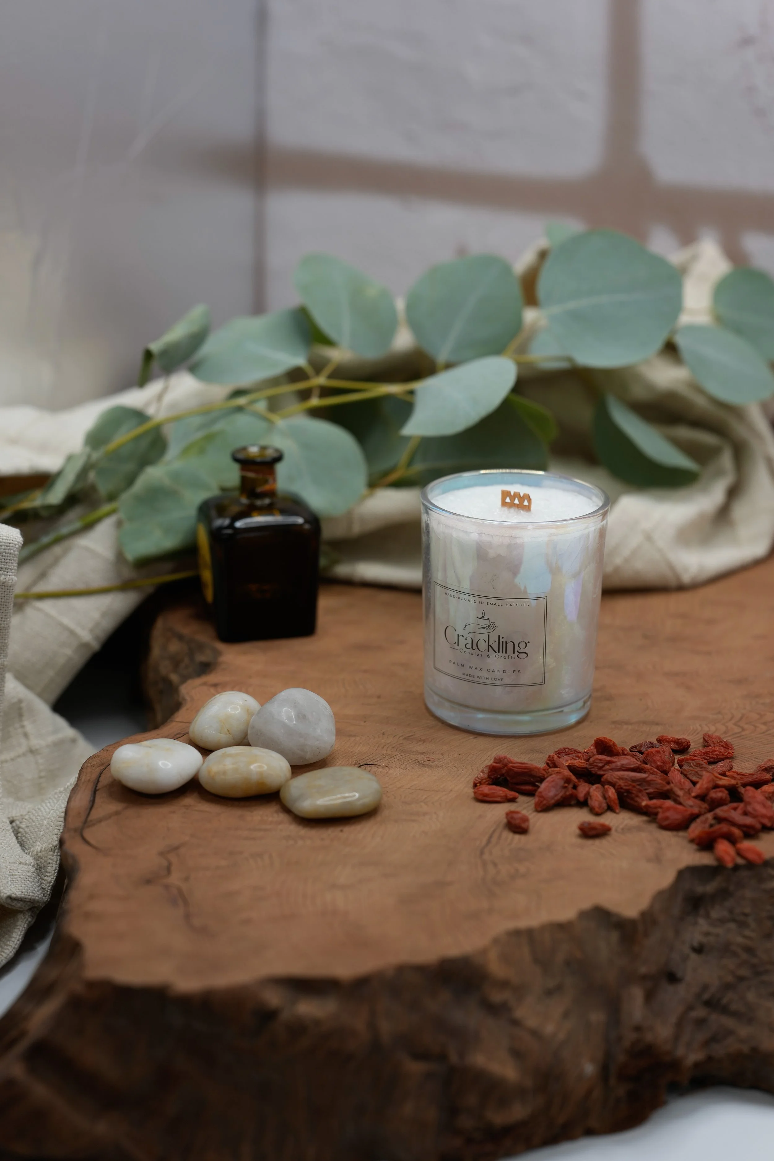 Angled view of a 6 oz Tobacco & Oud candle on a wood slab with eucalyptus, stones, and an amber bottle