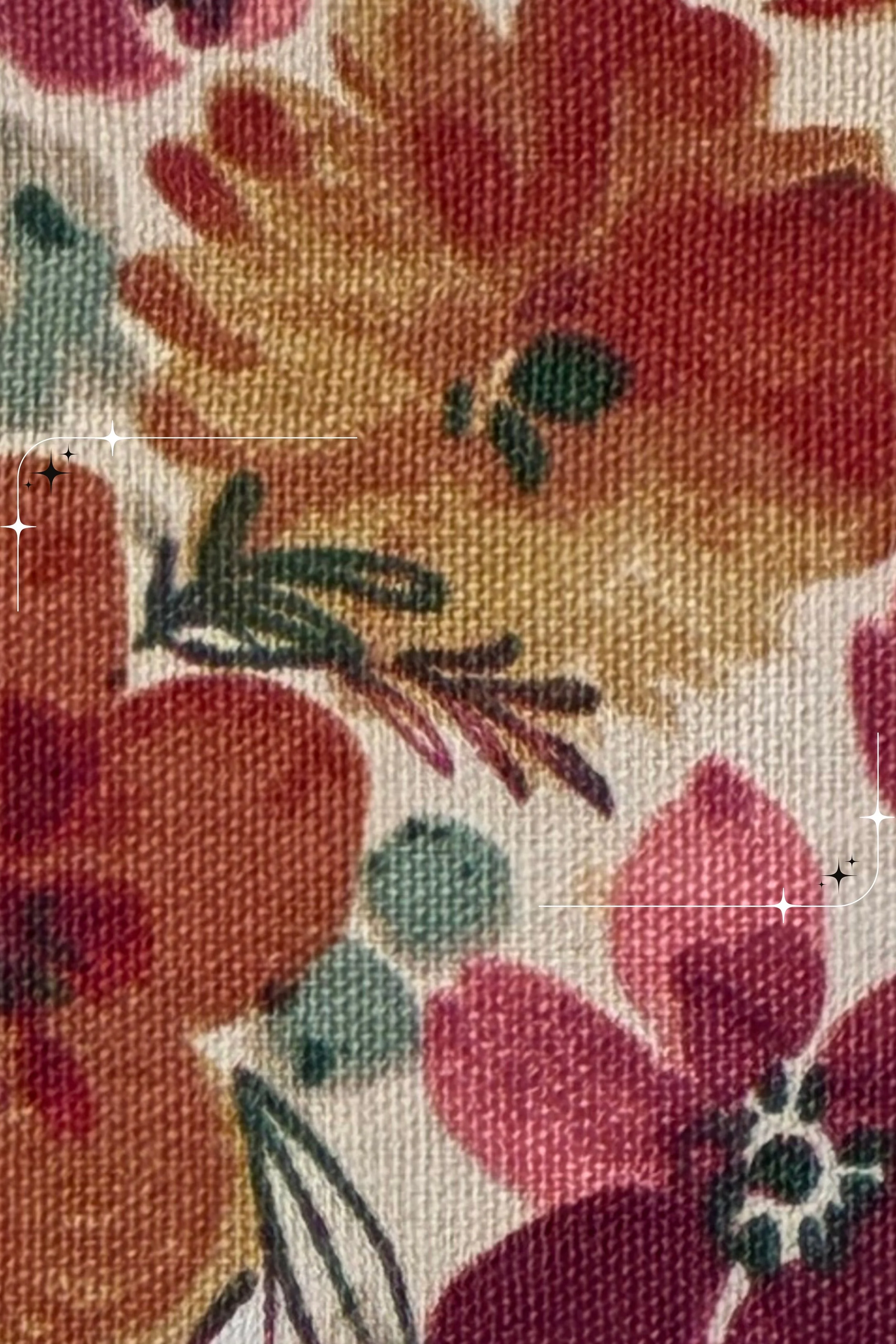 Close-up of cream cotton fabric with burgundy, orange, and golden flowers, green foliage, and decorative stitching.