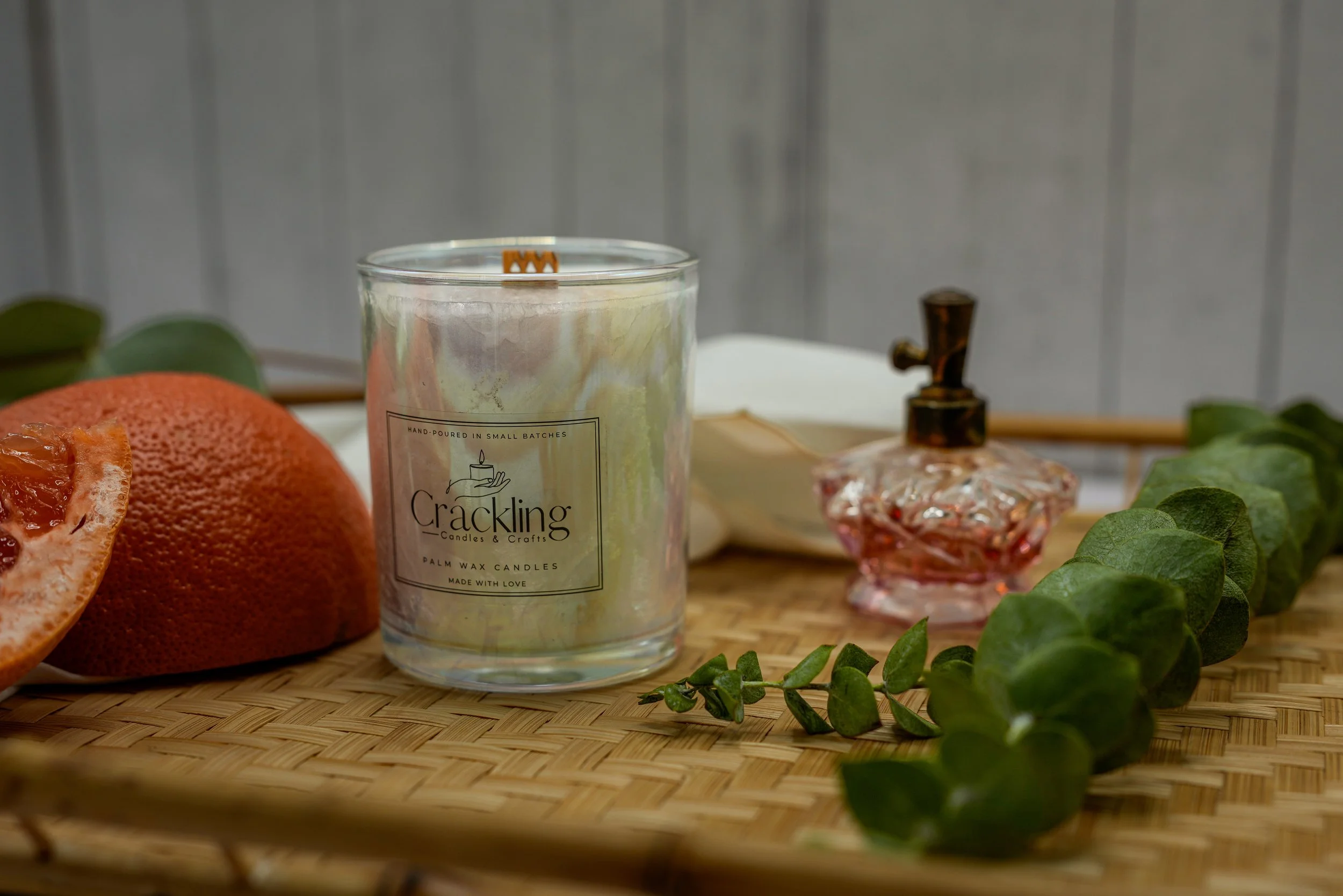 Pink Grapefruit palm wax candle in a clear glass jar, styled with grapefruit, greenery, and a small pink glass bottle.