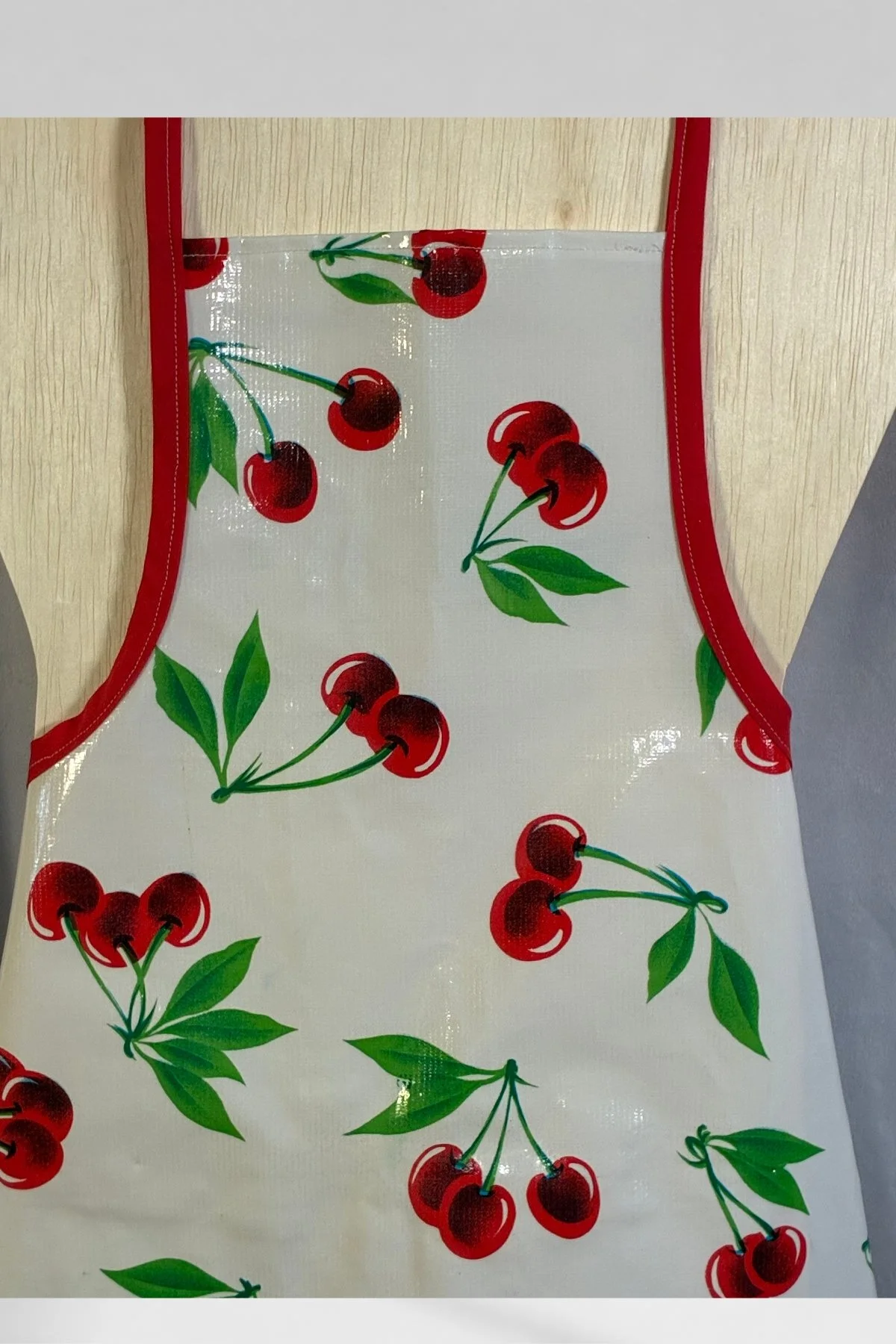 Close view of the children’s cherry-print oilcloth apron, showing the red edging and front pocket.