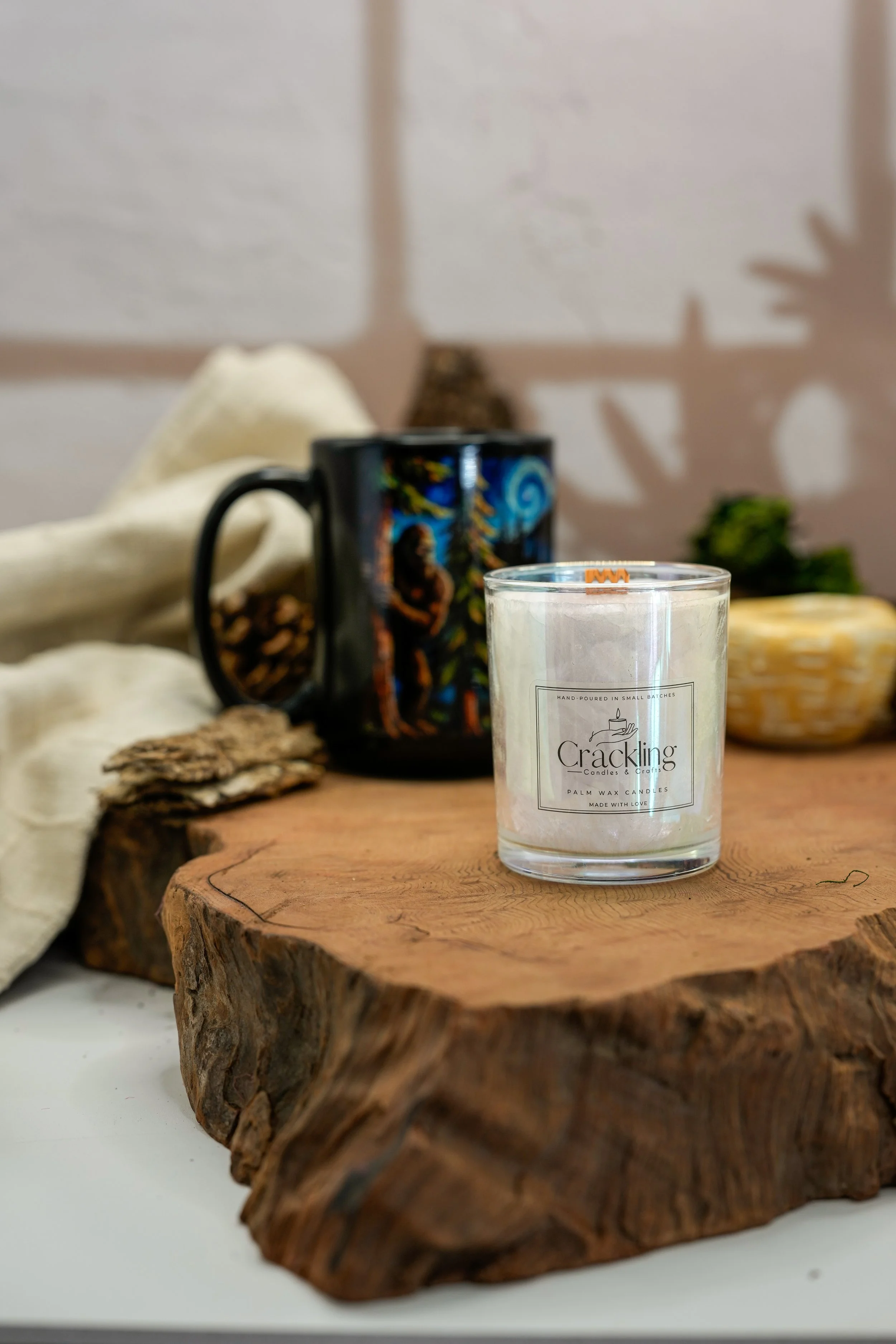 Caribbean Teakwood candle displayed on a rustic wood slab with a colorful tropical mug, cream linen, and natural accents.