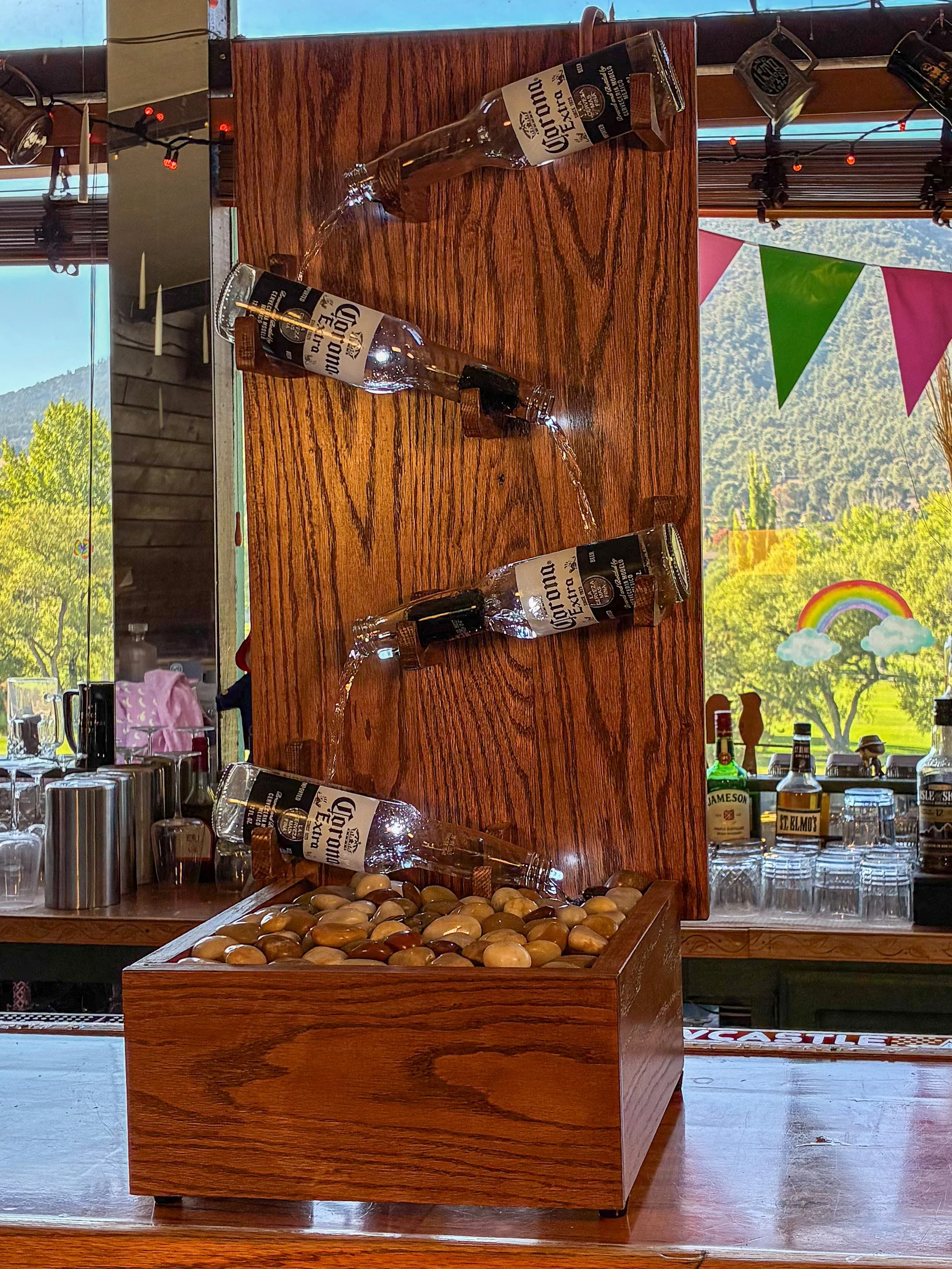 Red oak beer bottle fountain showing the cascading bottle arrangement and polished river rocks in the wooden basin.