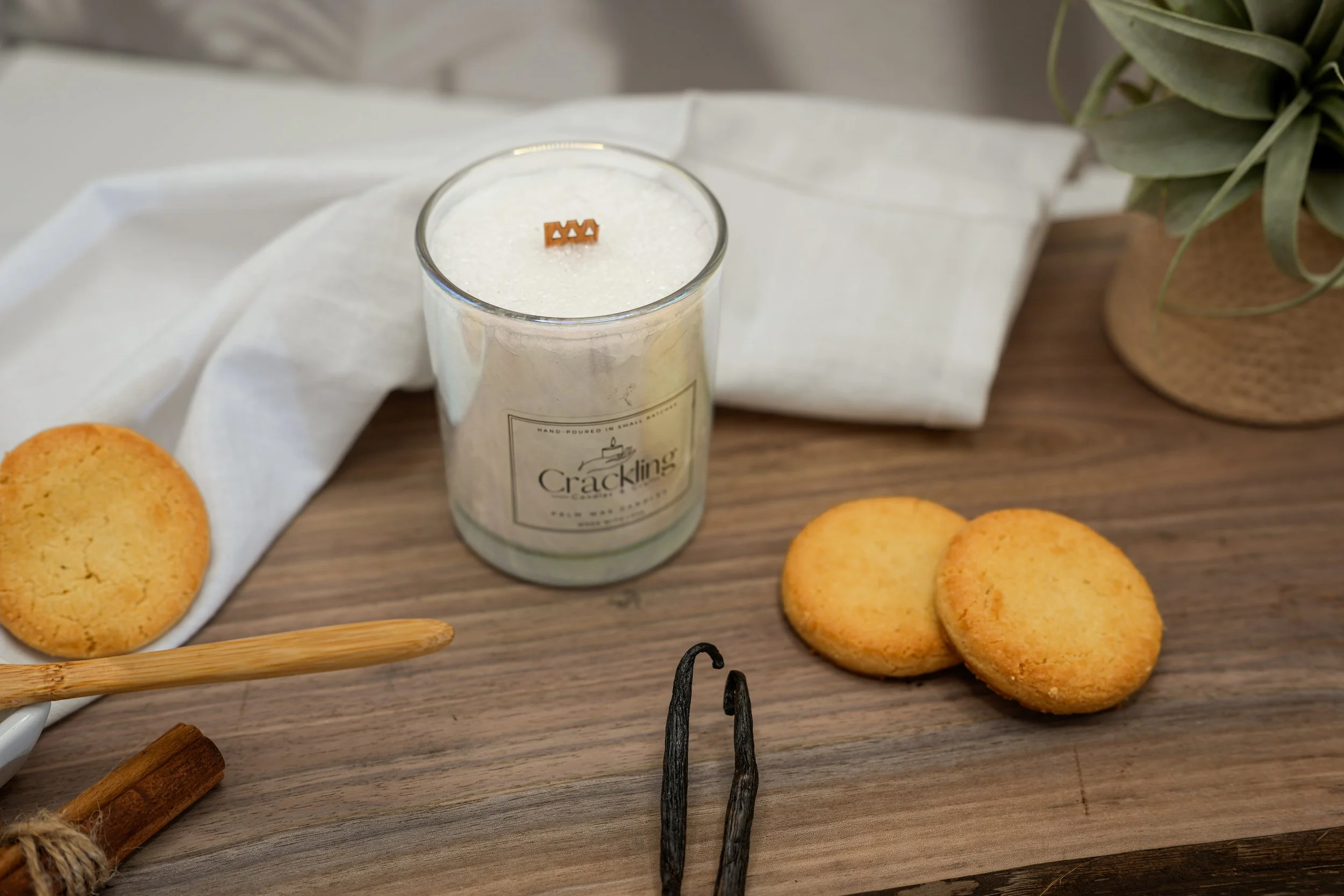 Sugar Cookie palm wax candle in a glass jar with a wooden wick, styled beside two cookies on a wooden surface.
