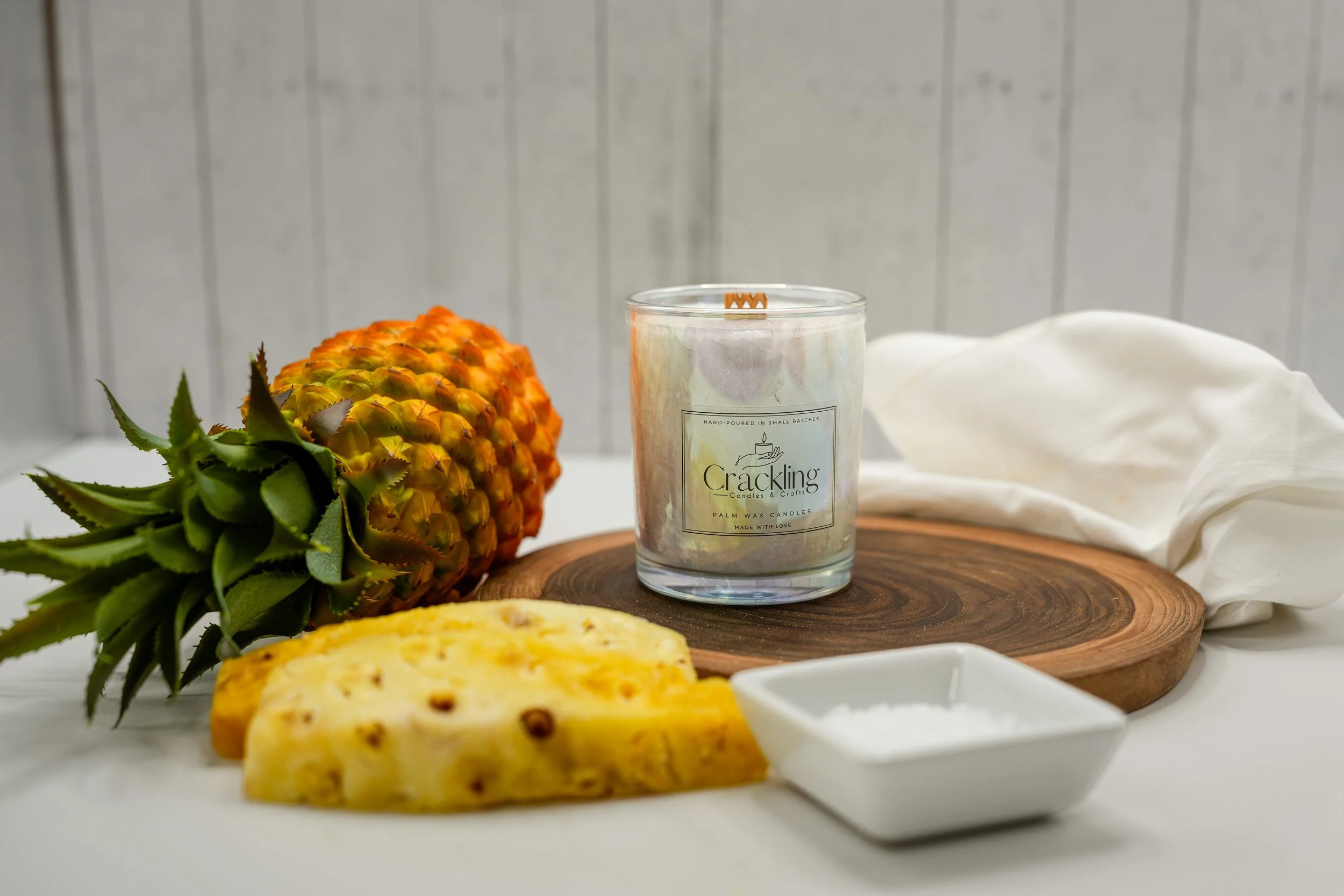 Iced Pineapple candle styled with pineapple slices, a whole pineapple, and white fabric
