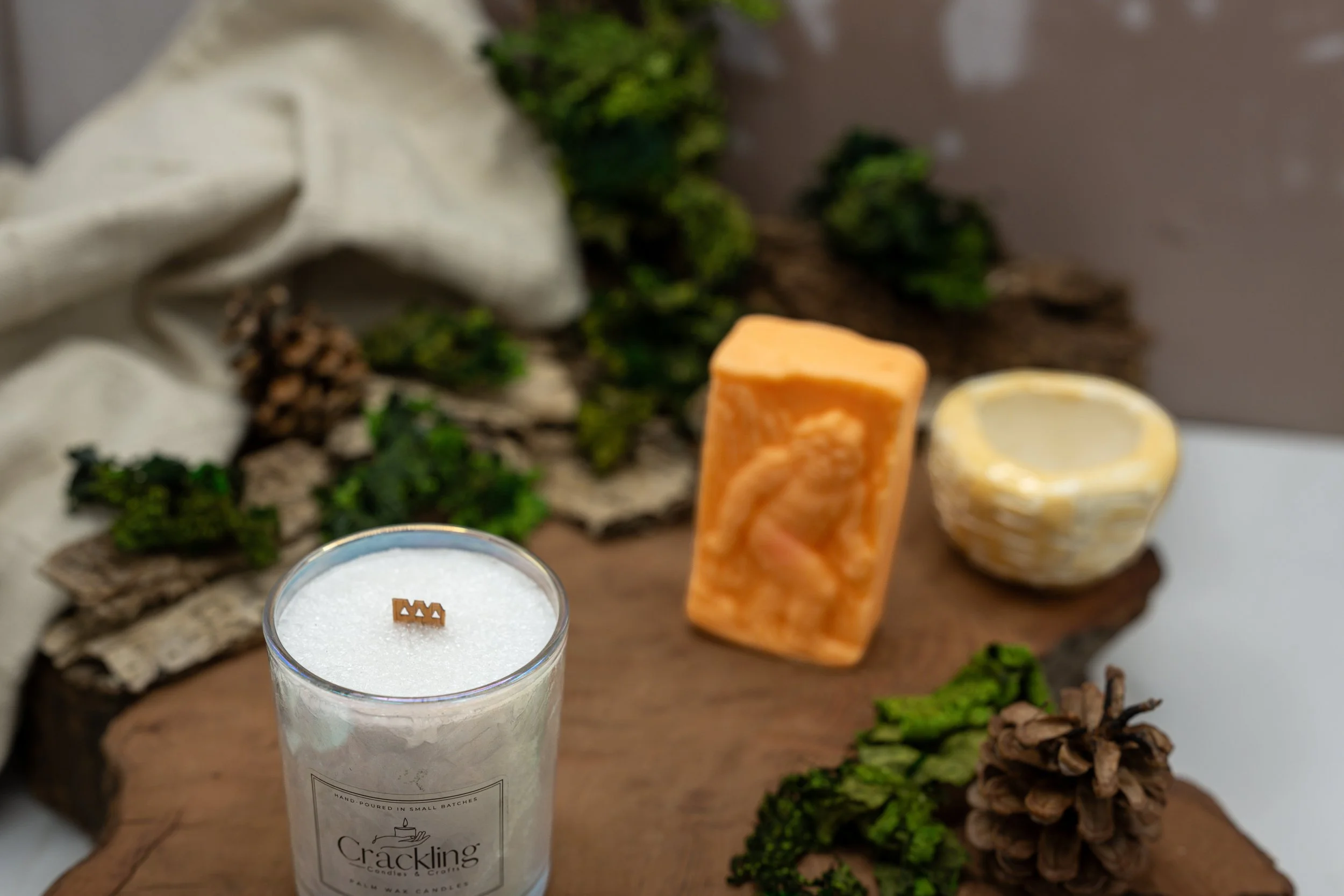 Top view of a Cardamom & Teakwood candle with a wooden wick, styled with greenery, pinecones, and warm natural decor.