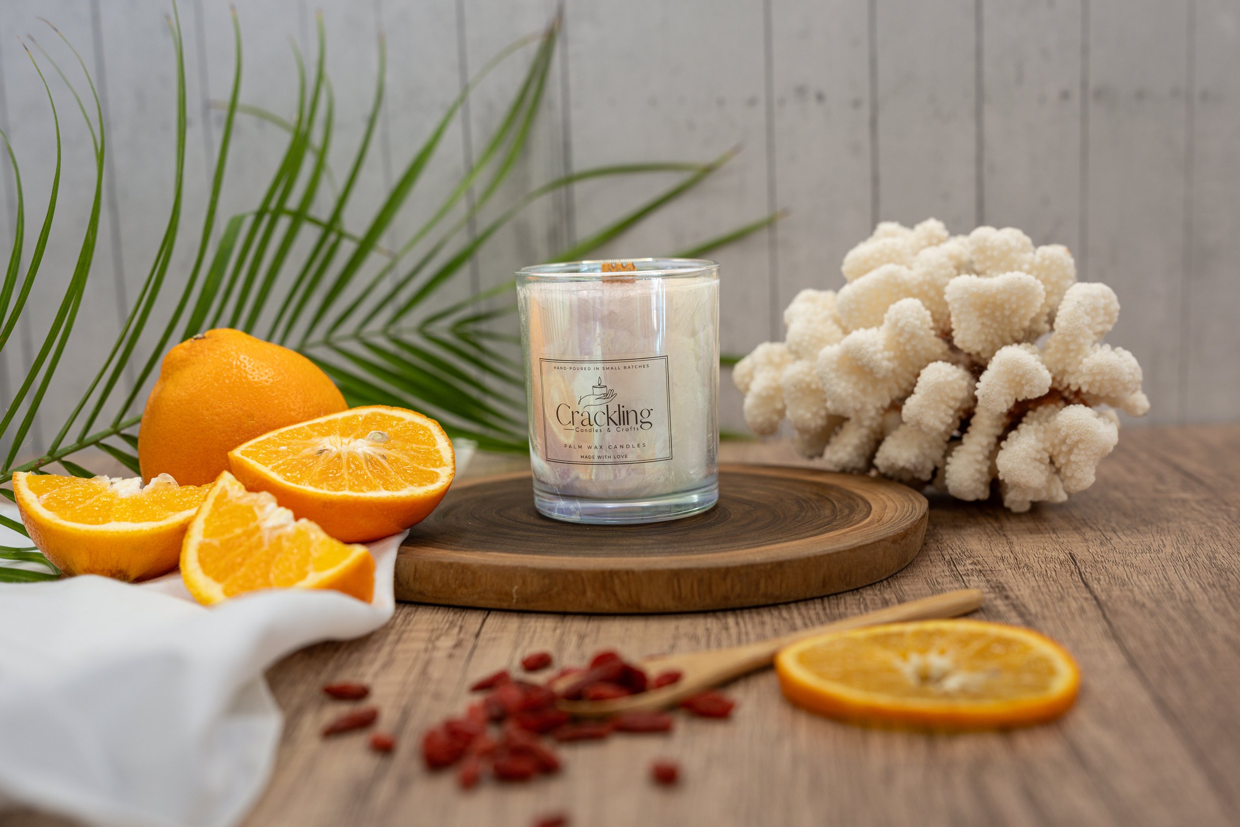 6 oz Bite Me palm wax candle with a wooden wick, styled with fresh orange slices, tropical greenery, and dried botanicals.