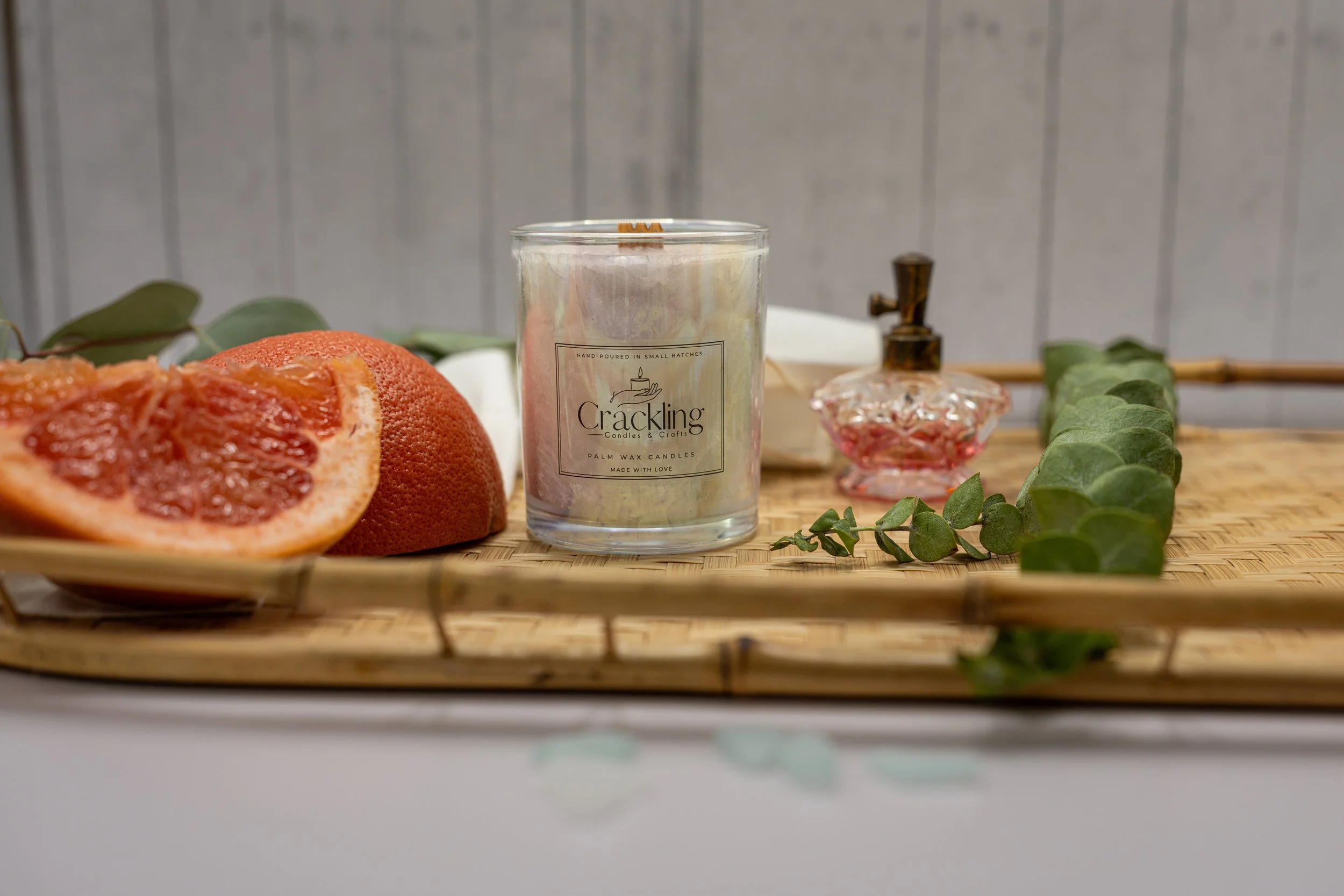 Pink Grapefruit palm wax candle centered on a wooden board with cut grapefruit, greenery, and a pink glass bottle.