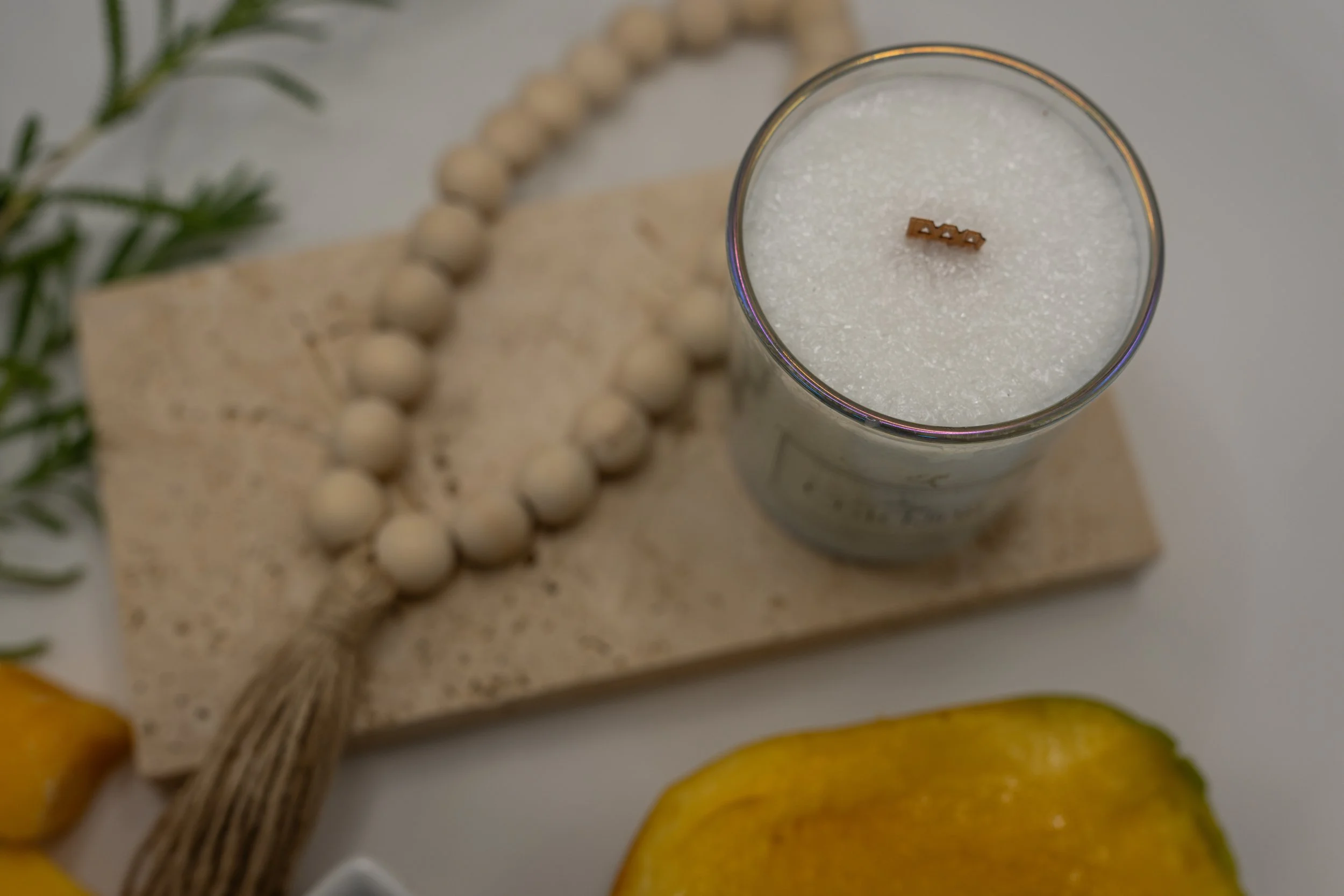 Top view of Mango Papaya palm wax candle showing its crystalline wax and wooden wick beside wooden beads and cut fruit.