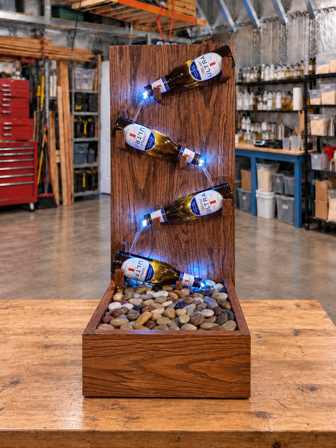 Red oak fountain with four Michelob Ultra bottles, illuminated LED lights, and a river rock basin on a wooden workbench.