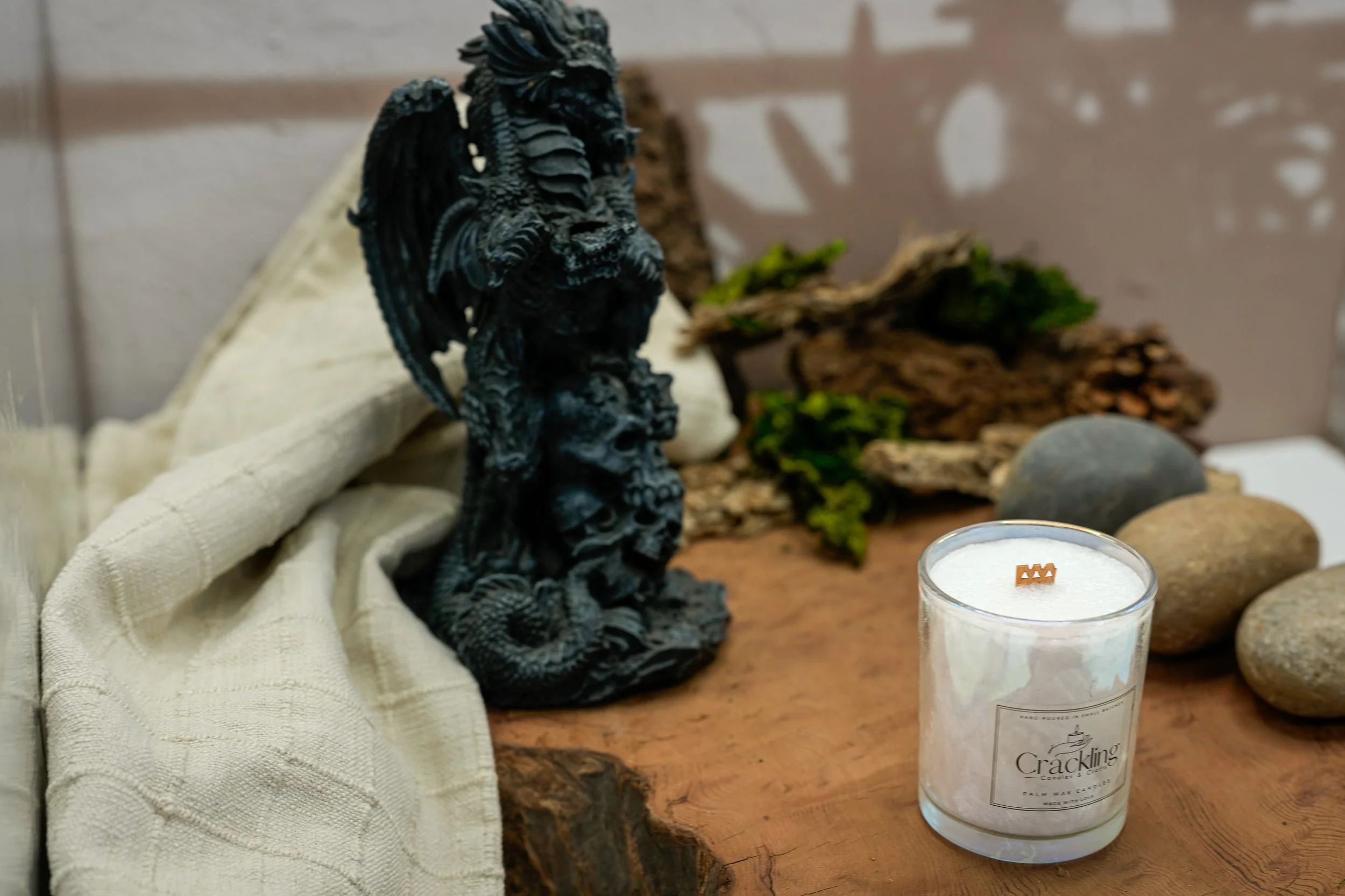 Dragon’s Blood candle in a clear glass jar beside a black dragon figurine, with moss and natural wood in a close-up styled display.