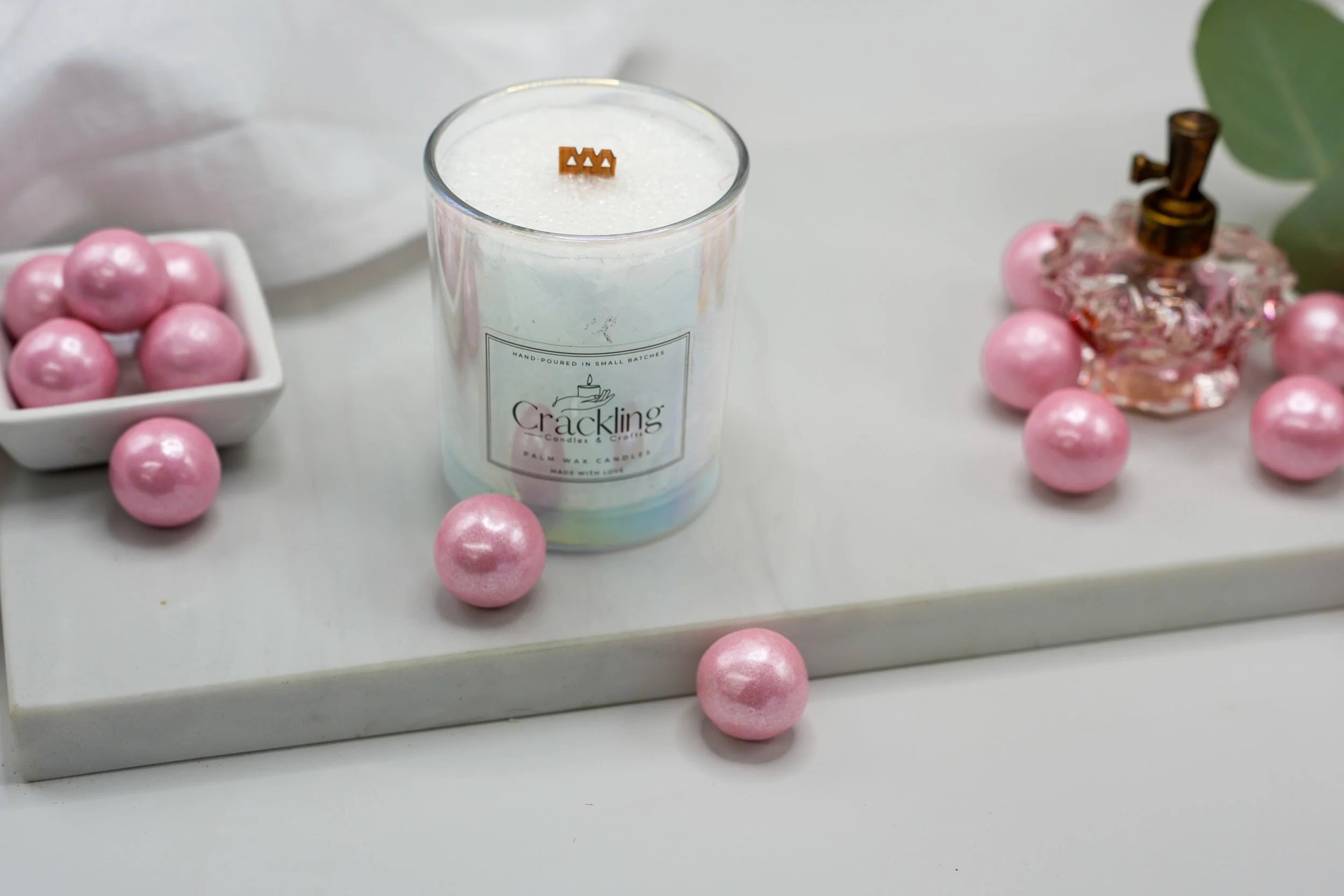 Bubble Gum candle styled on a white riser with pink gumballs and soft white linen against a warm neutral backdrop.